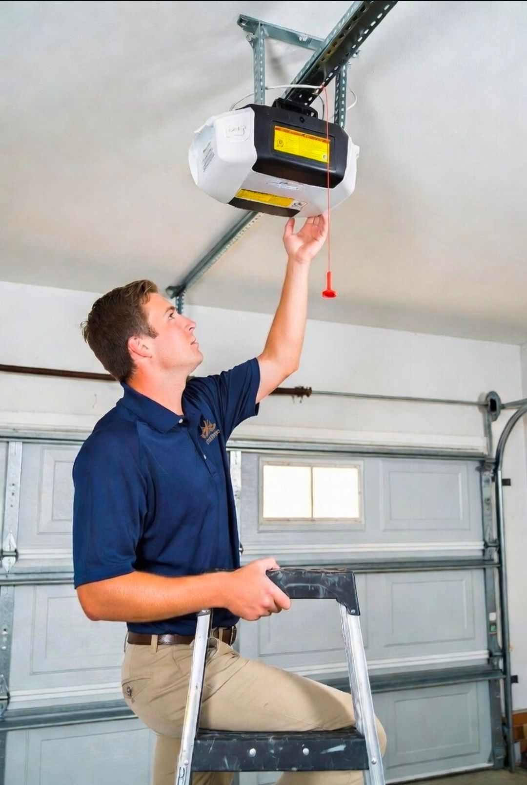 Man on ladder adjusting a garage door opener in a garage.