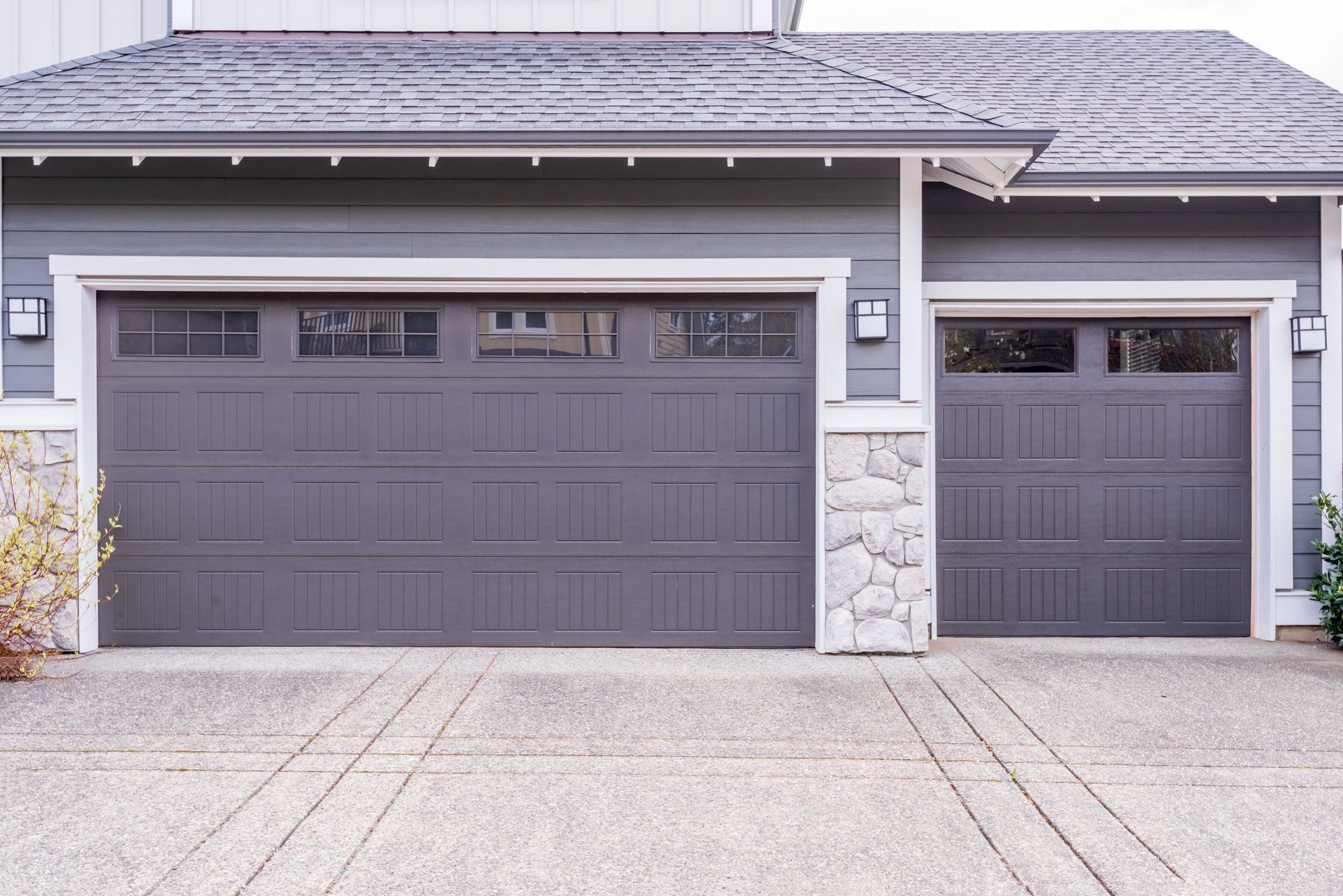 Gray garage doors on a gray house with a stone column, set on a concrete driveway.