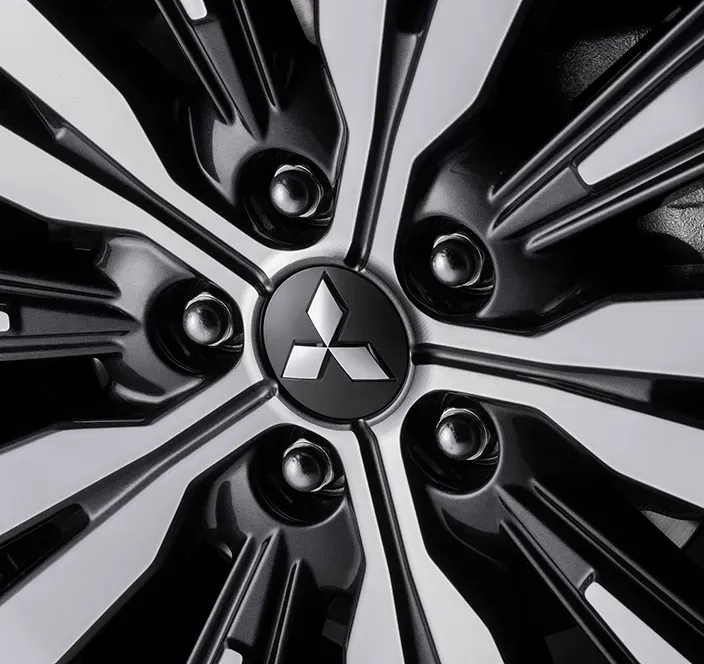 Detalhe da roda de um carro Mitsubishi com um design preto e prateado e o logotipo da empresa no centro.