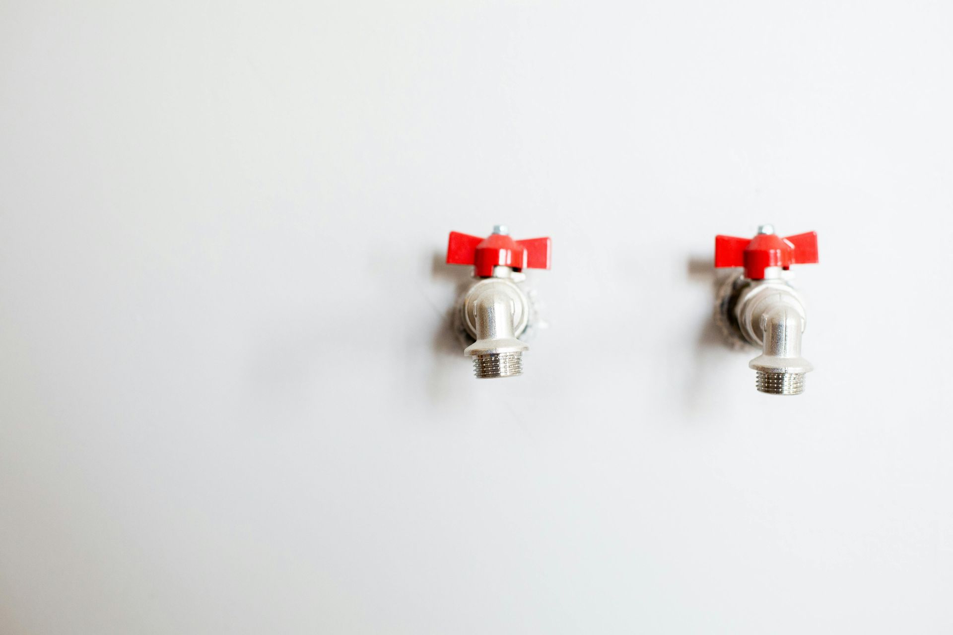 Two water faucets with red handles on a white wall.