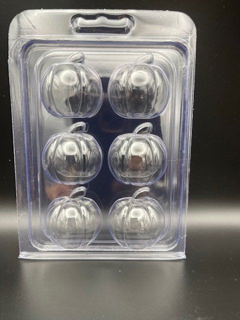 A clear plastic container filled with pumpkins is sitting on a table.