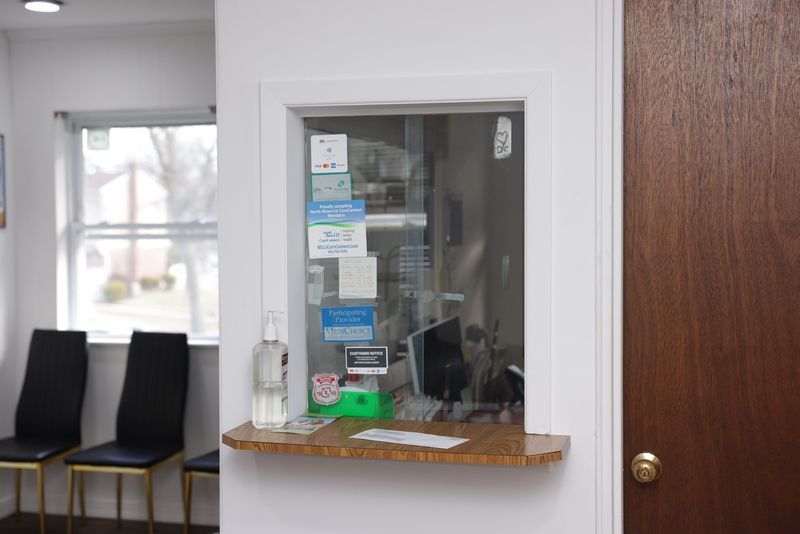 Reception window in a medical office; hand sanitizer, papers, and signage on a wooden counter.