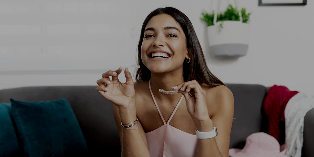 Woman with dark skin smiles, touching face; beige background.