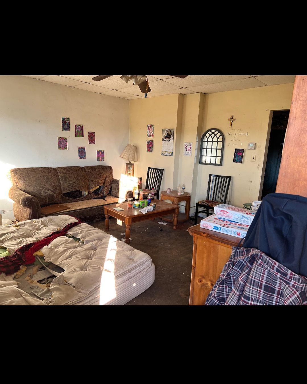 A cluttered, damaged living room with a couch, mattress, coffee table, and various debris