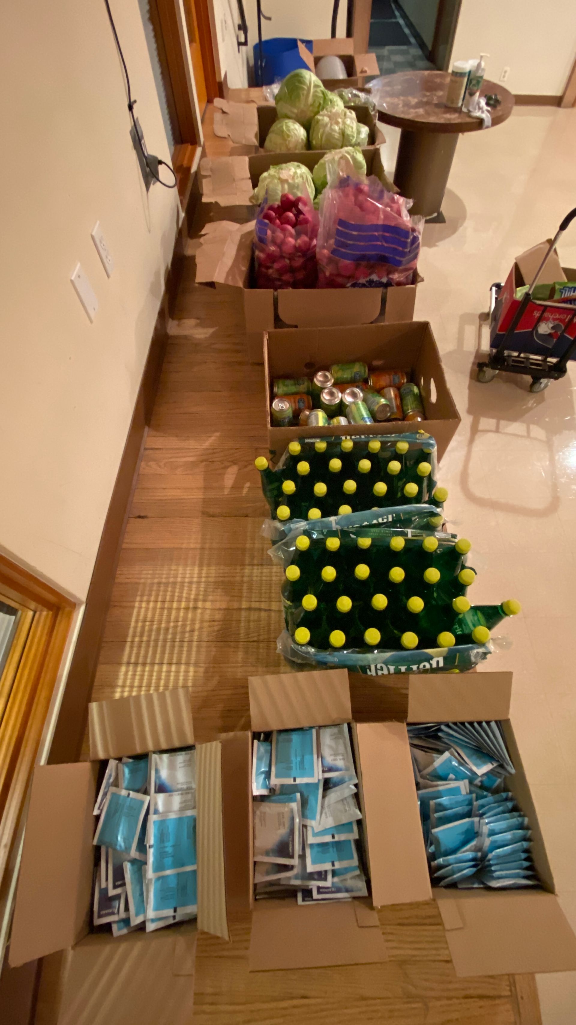 A row of boxes filled with vegetables and face masks on a wooden floor.