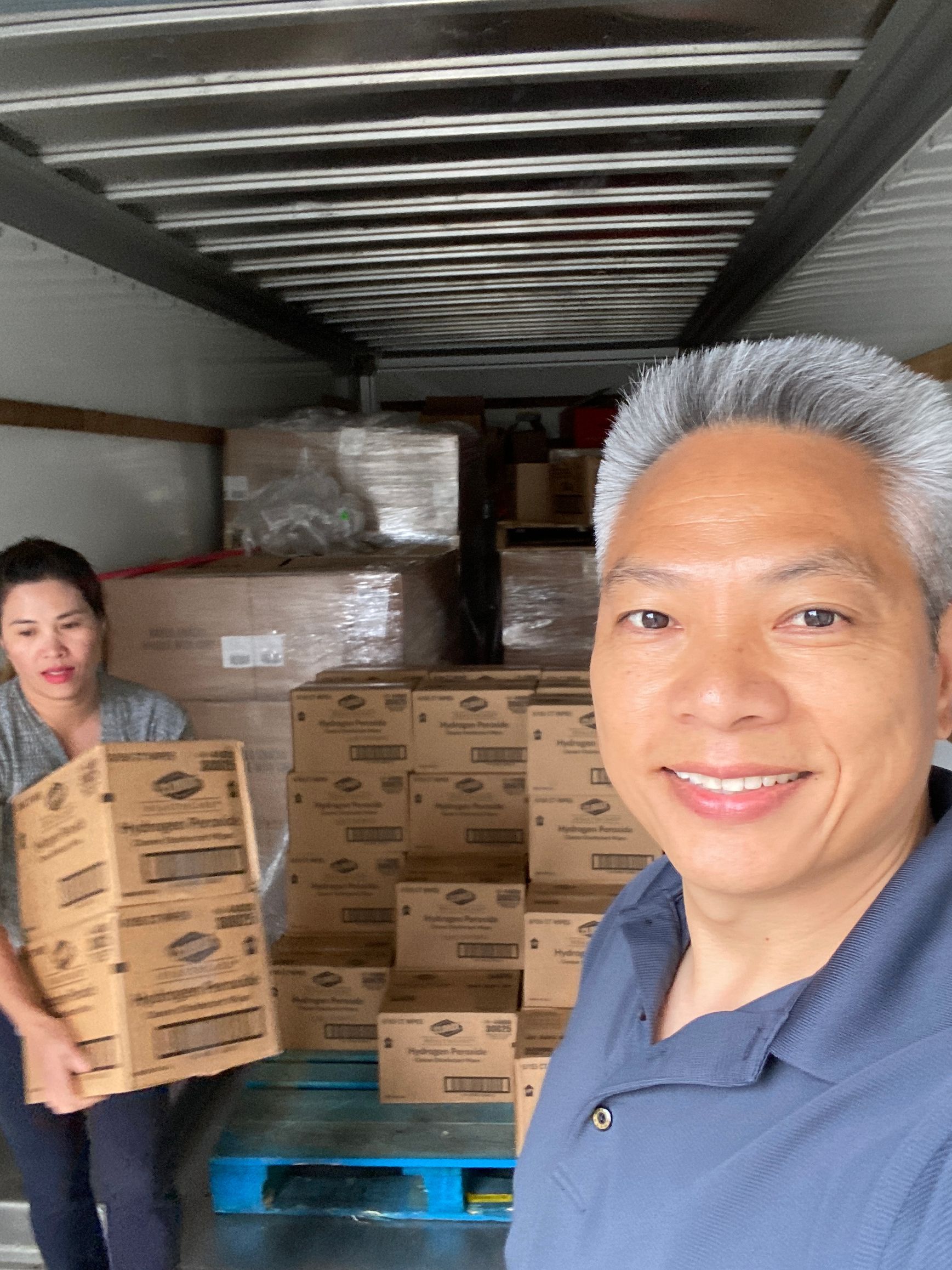 A man and a woman are standing in the back of a truck holding boxes.