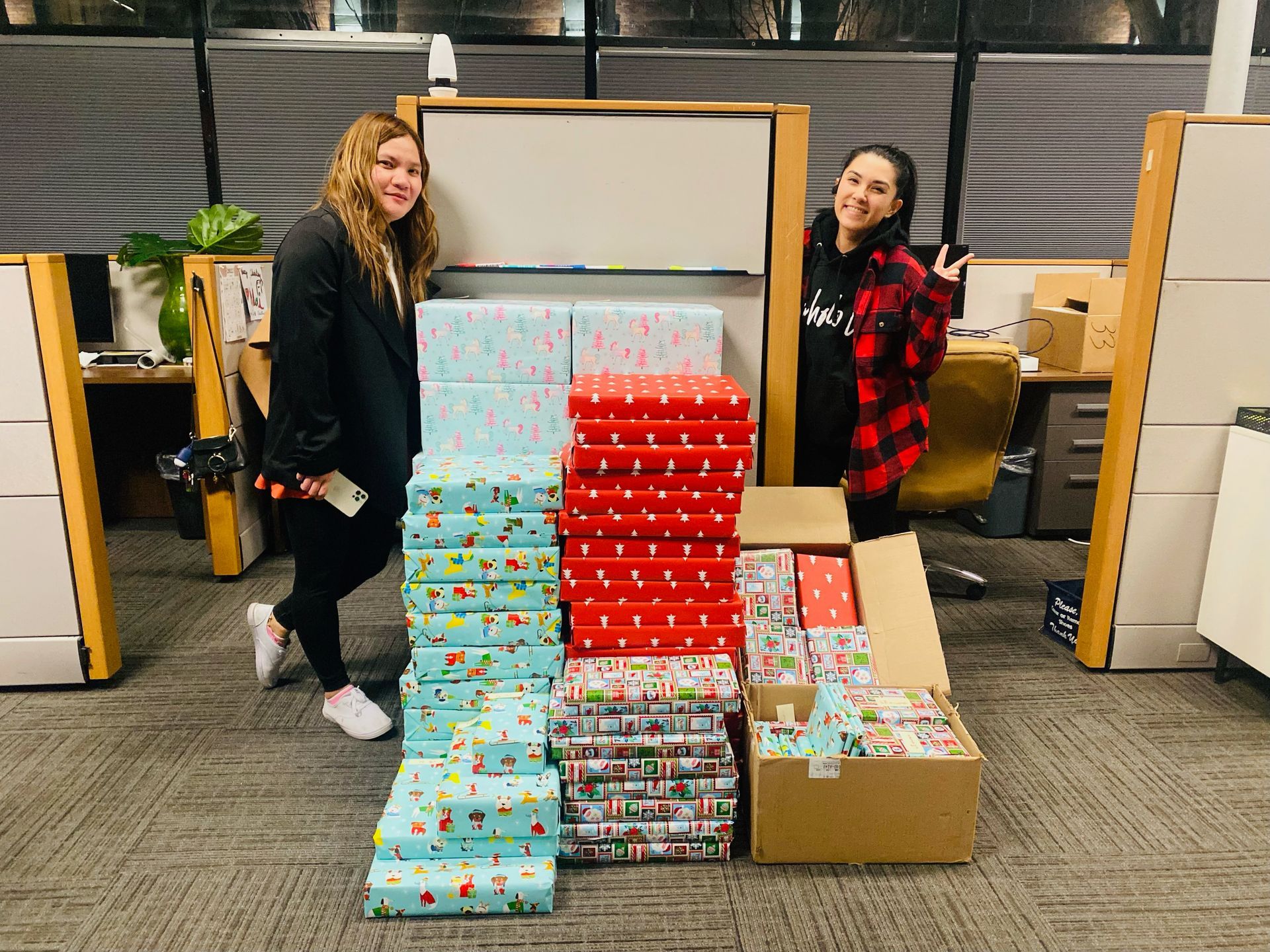 Two women are standing in front of a pile of wrapped gifts.