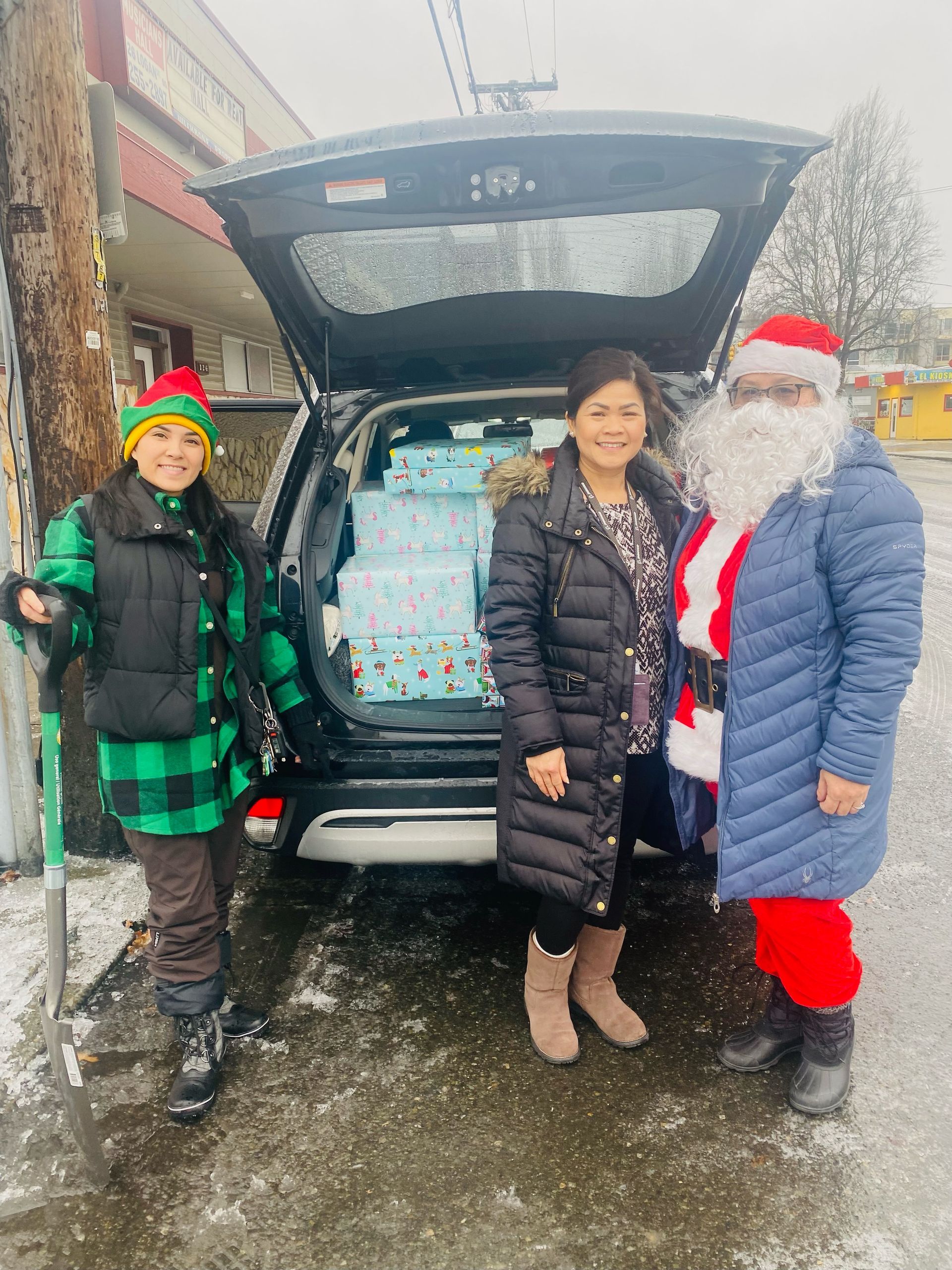 A group of people standing next to a car with gifts in the back.