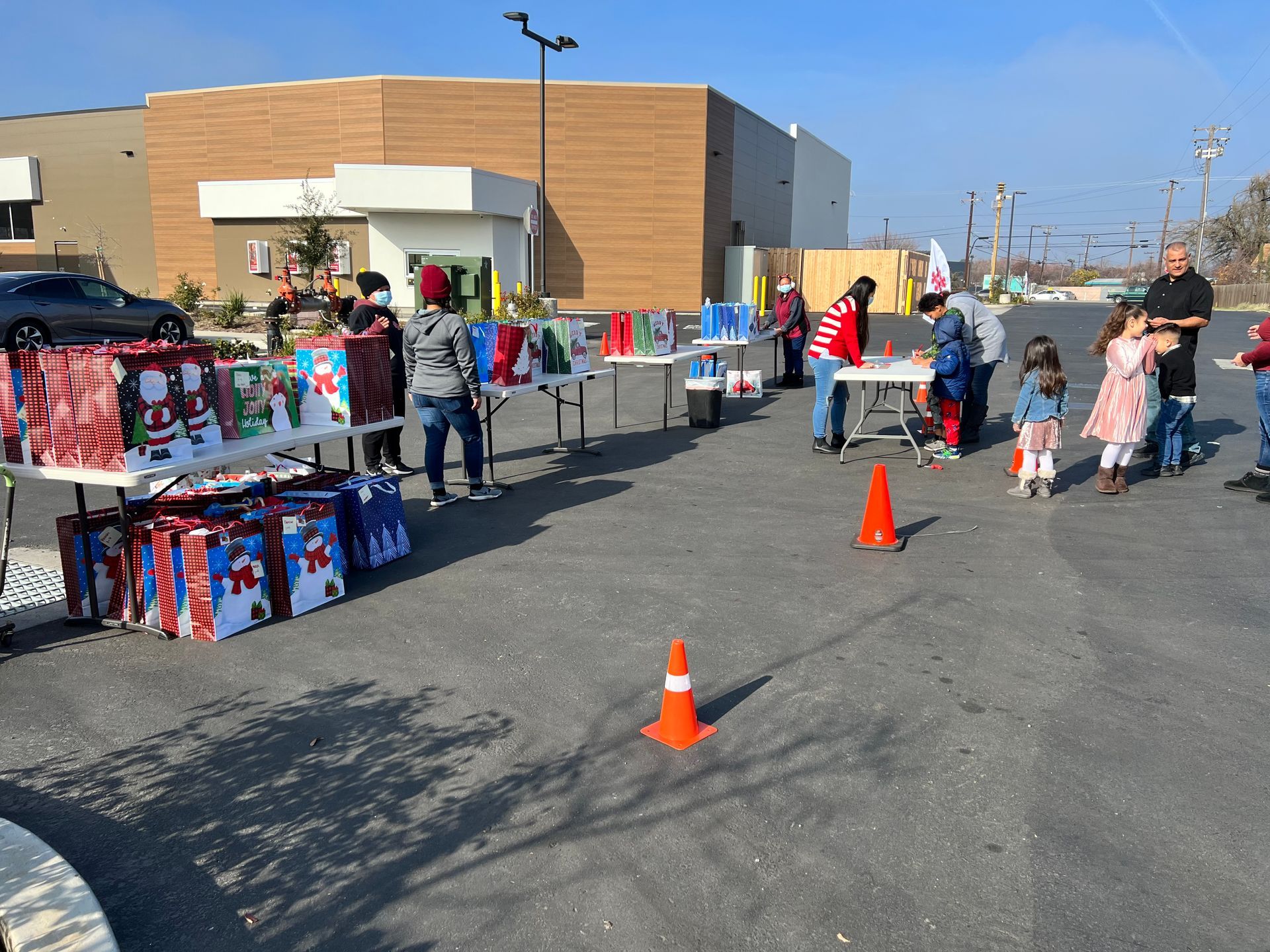 A group of people are standing around tables with gifts on them in a parking lot.