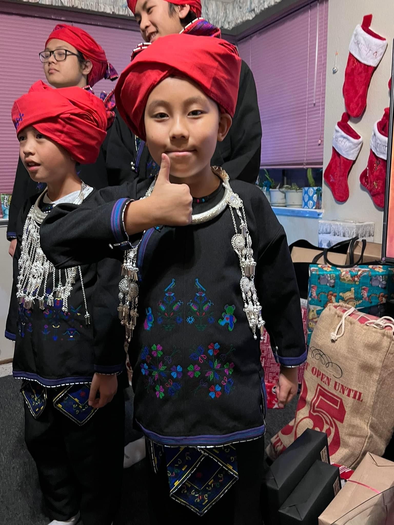 A group of children wearing red turbans are standing next to each other giving a thumbs up.