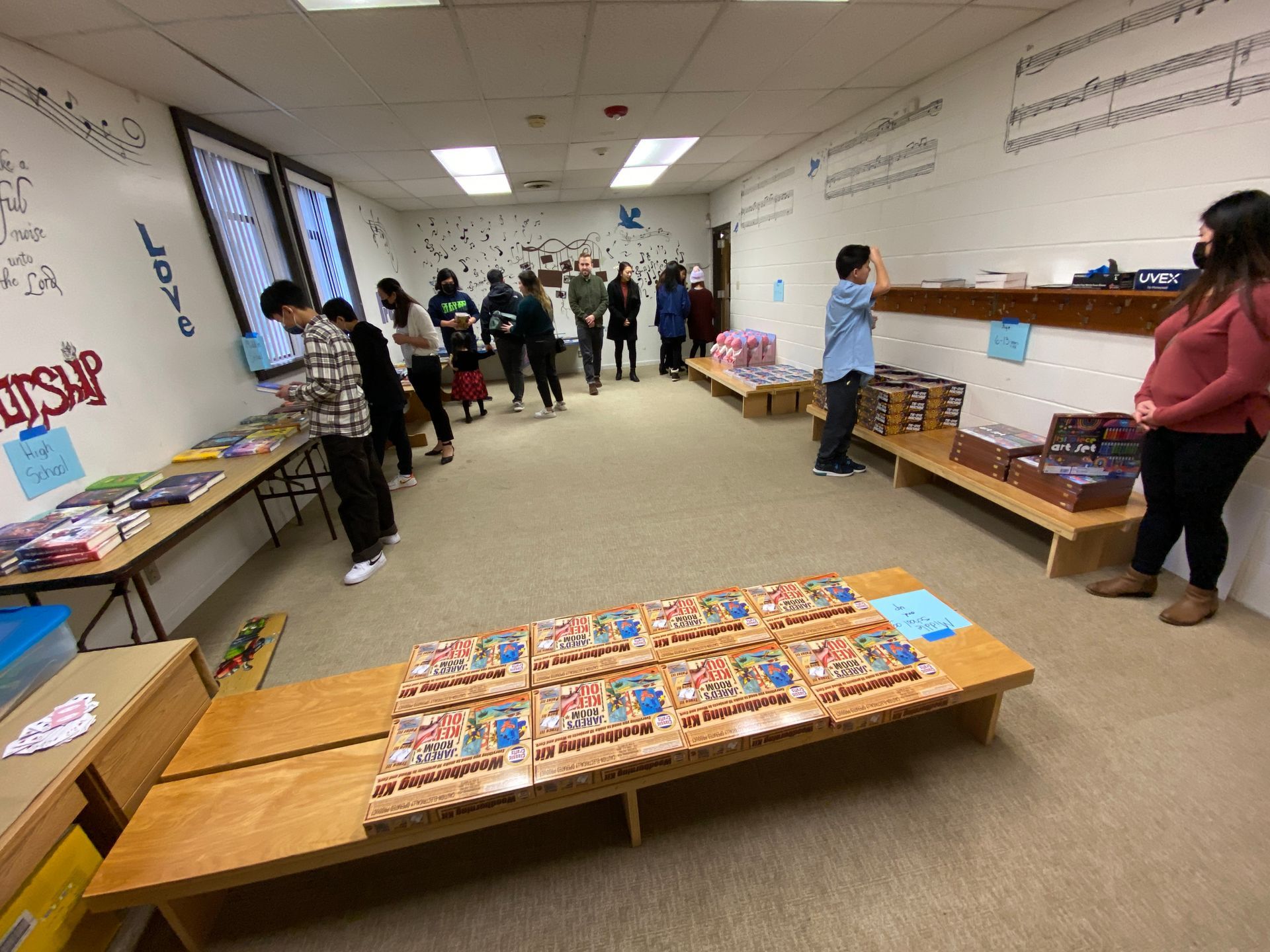 A group of people are standing in a room with tables and benches.