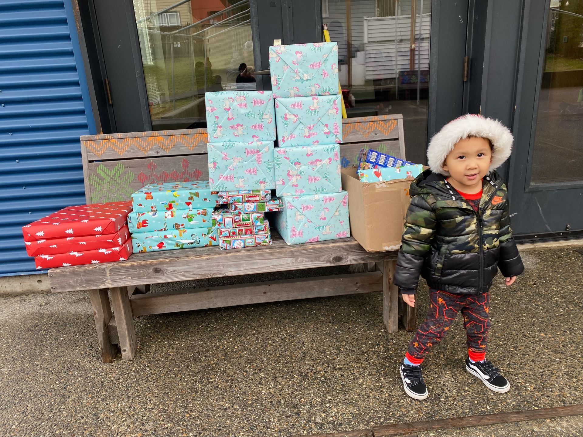 A little boy is standing in front of a wooden bench filled with gifts.