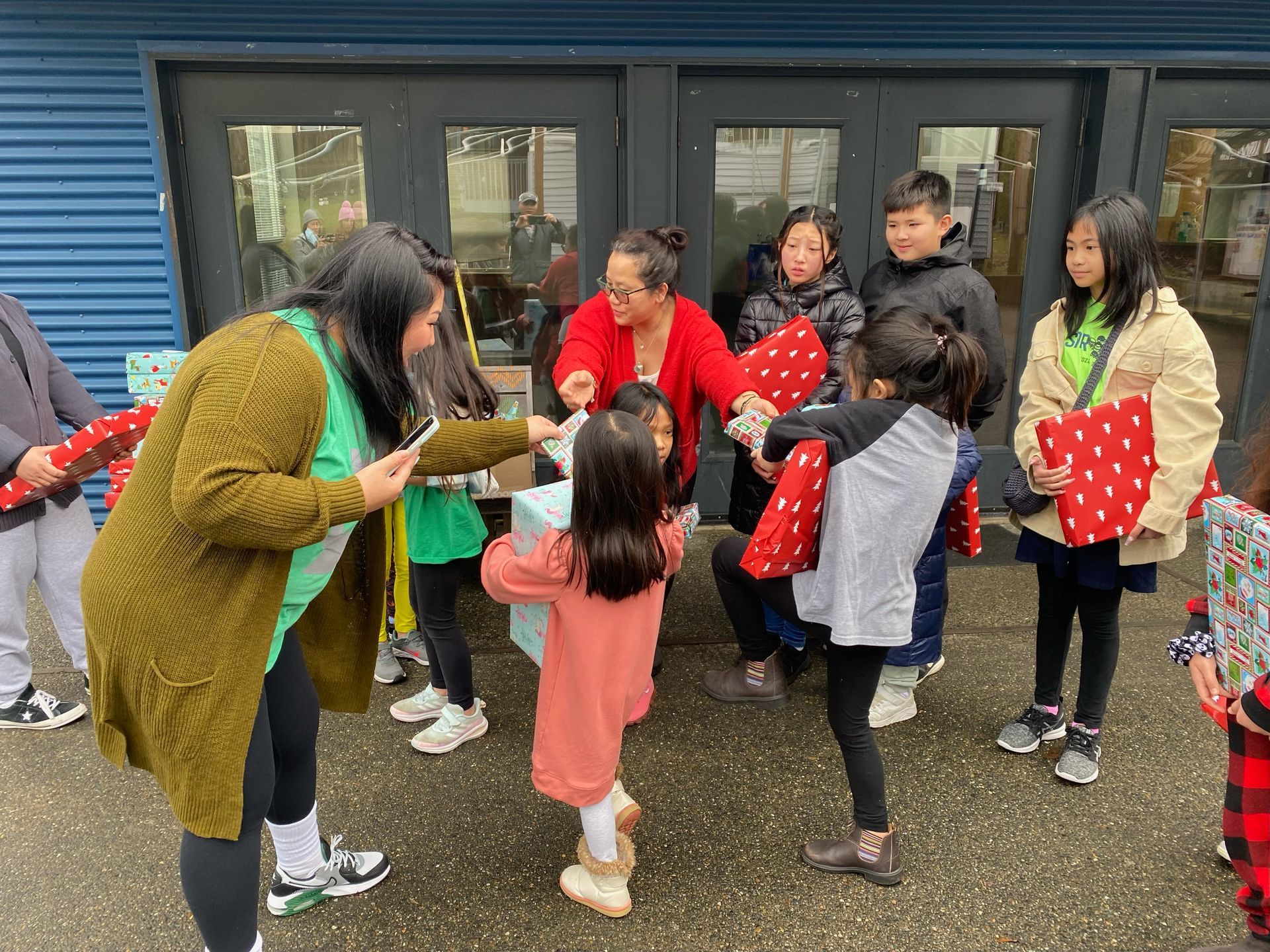 A group of children are standing in front of a building holding presents.