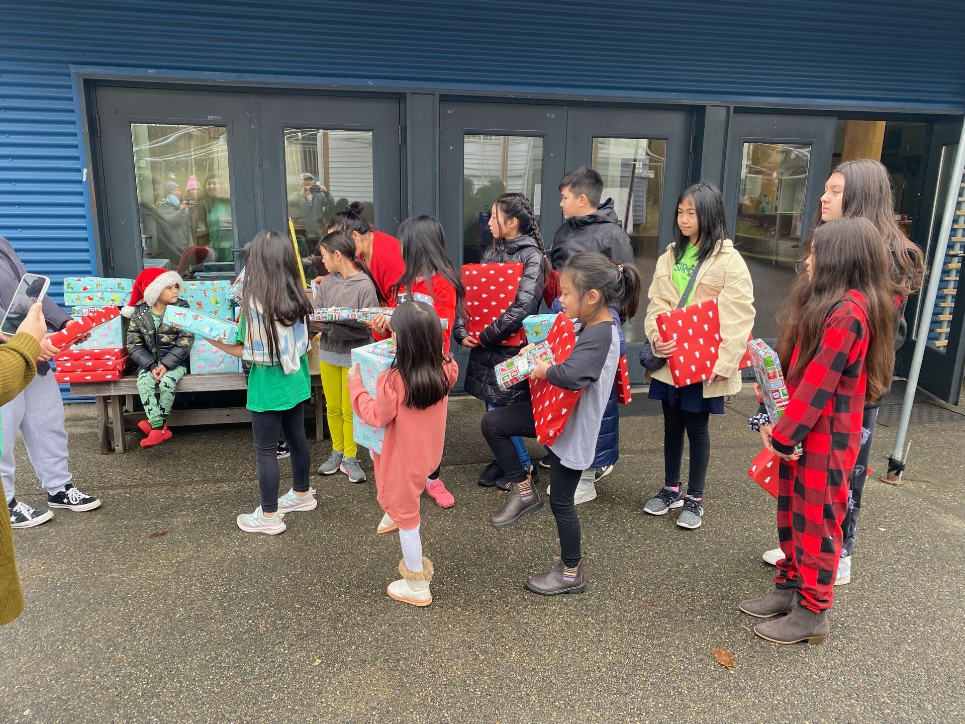 A group of children are standing in front of a building holding presents.