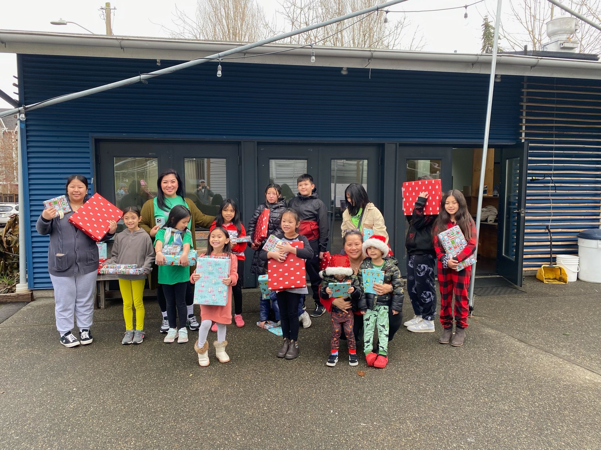 A group of children are standing in front of a building holding presents.