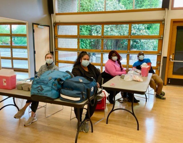 A group of people wearing face masks are sitting at tables in a room.