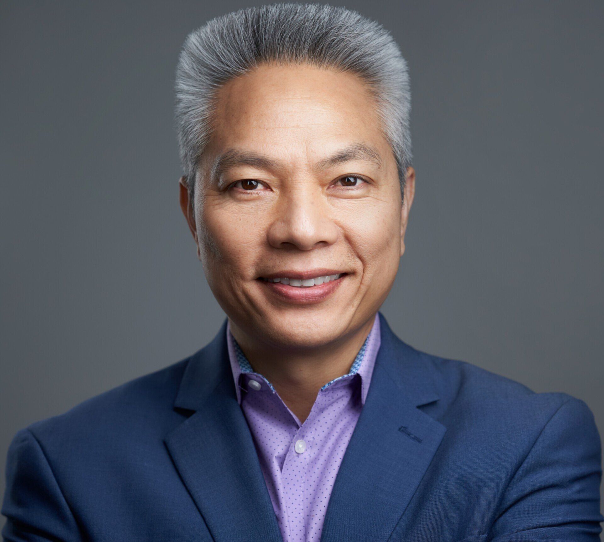 A man in a blue suit and purple shirt is smiling for the camera.