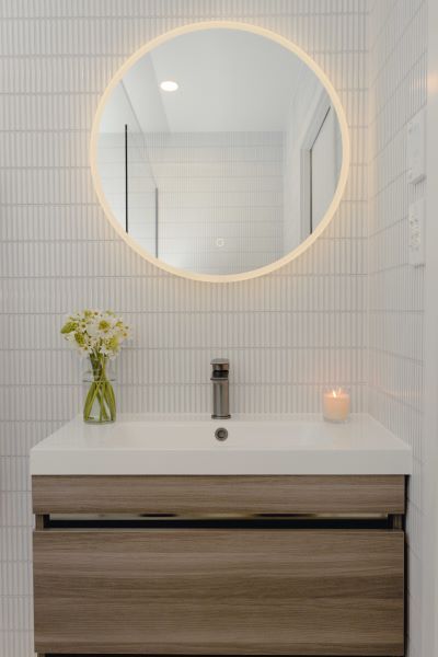 A bathroom sink with a round mirror and a vase of flowers on it.