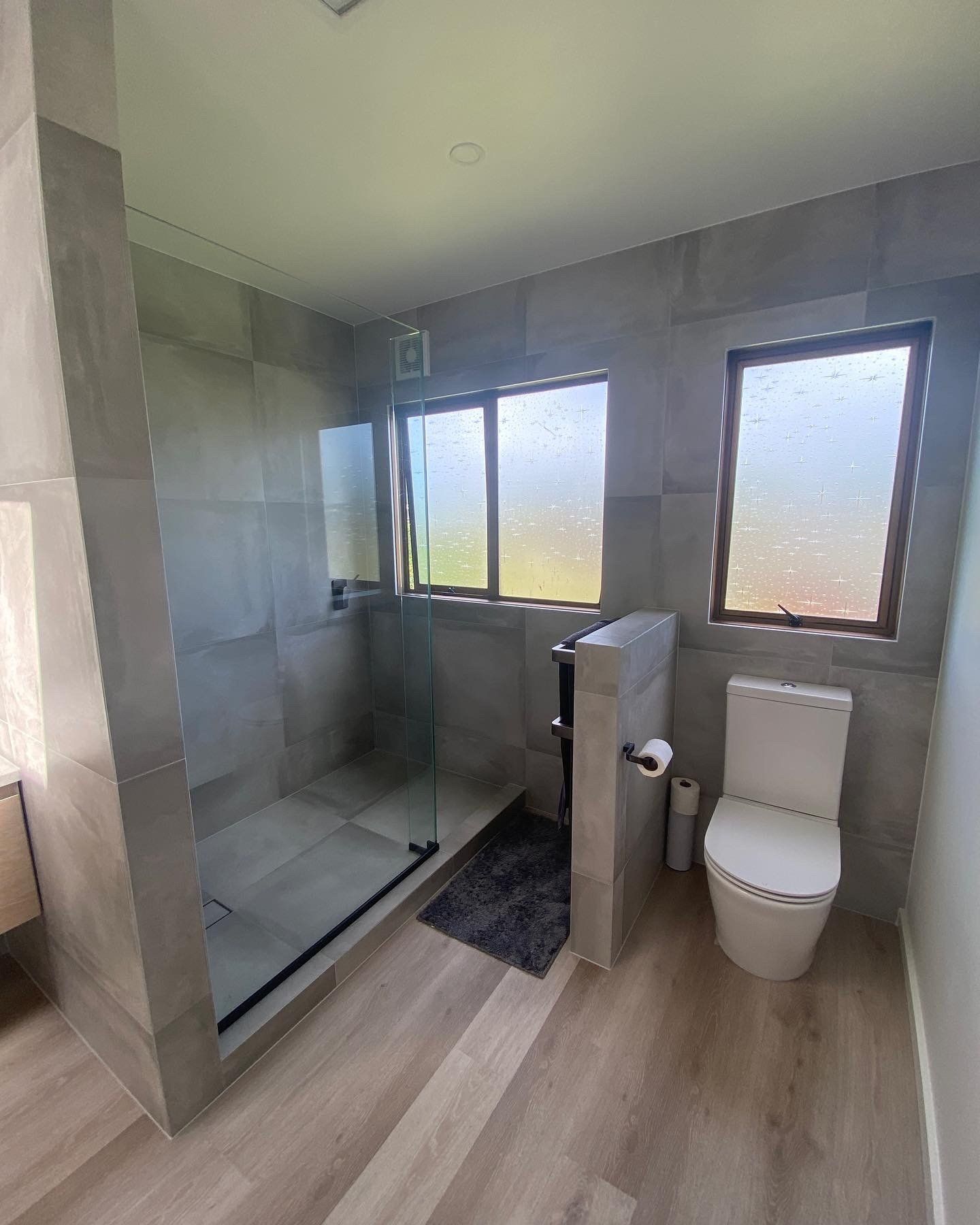 A bathroom with a toilet , shower and window.