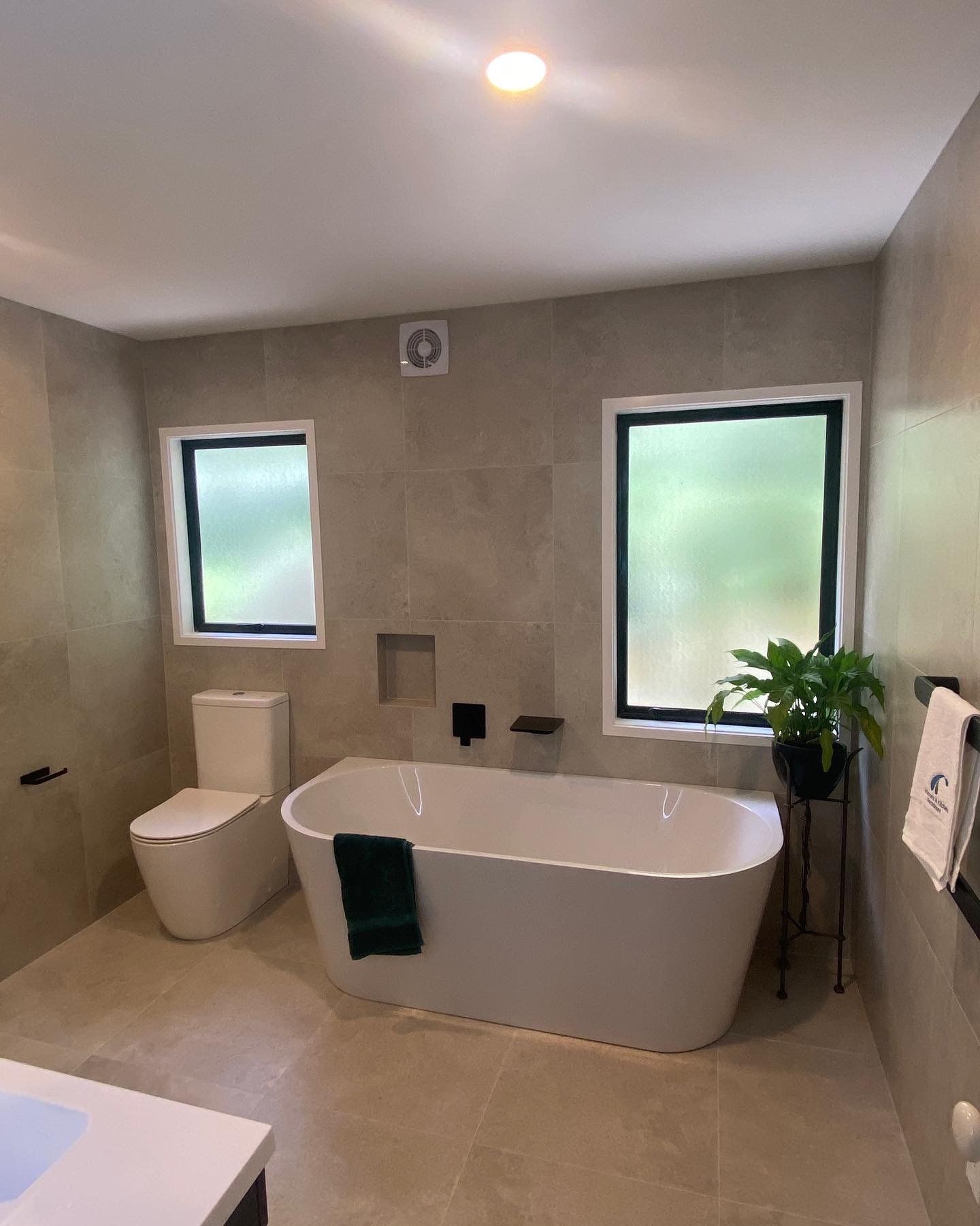 A bathroom with a bathtub , toilet , sink and two windows.