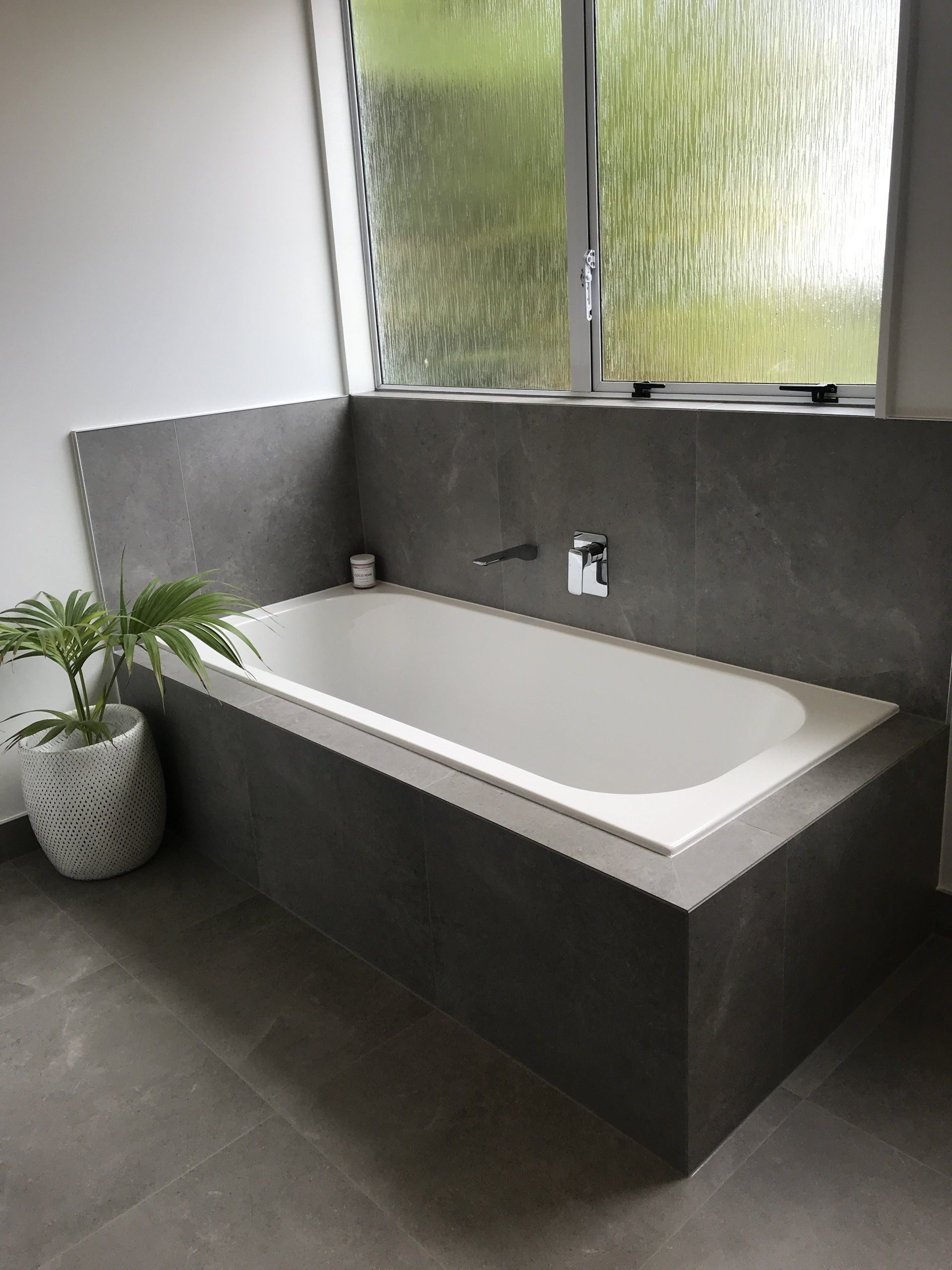 A bathtub in a bathroom next to a window and a potted plant.
