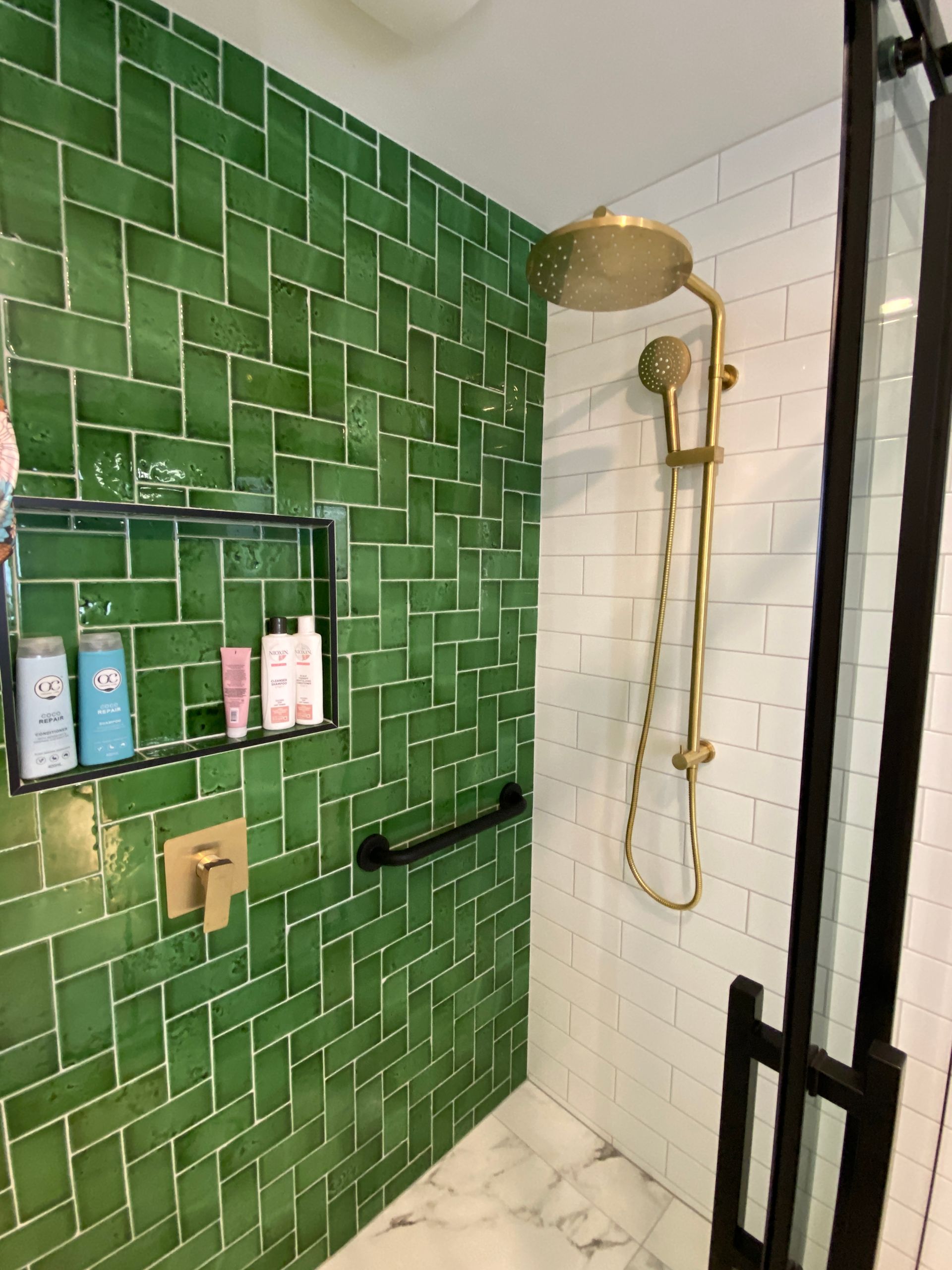 A bathroom with green tiles and a brass shower head.
