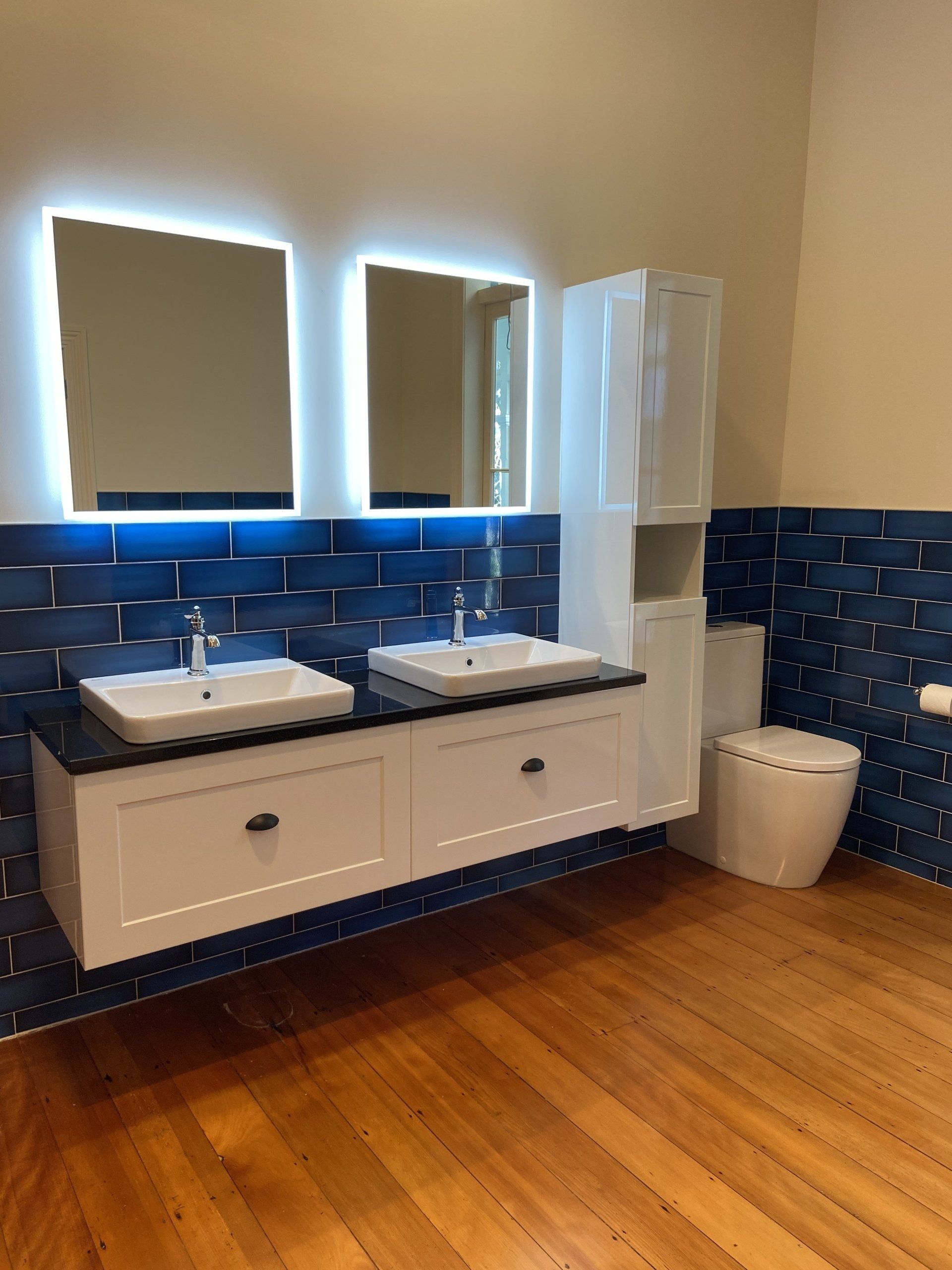 A bathroom with two sinks , a toilet , and two mirrors.