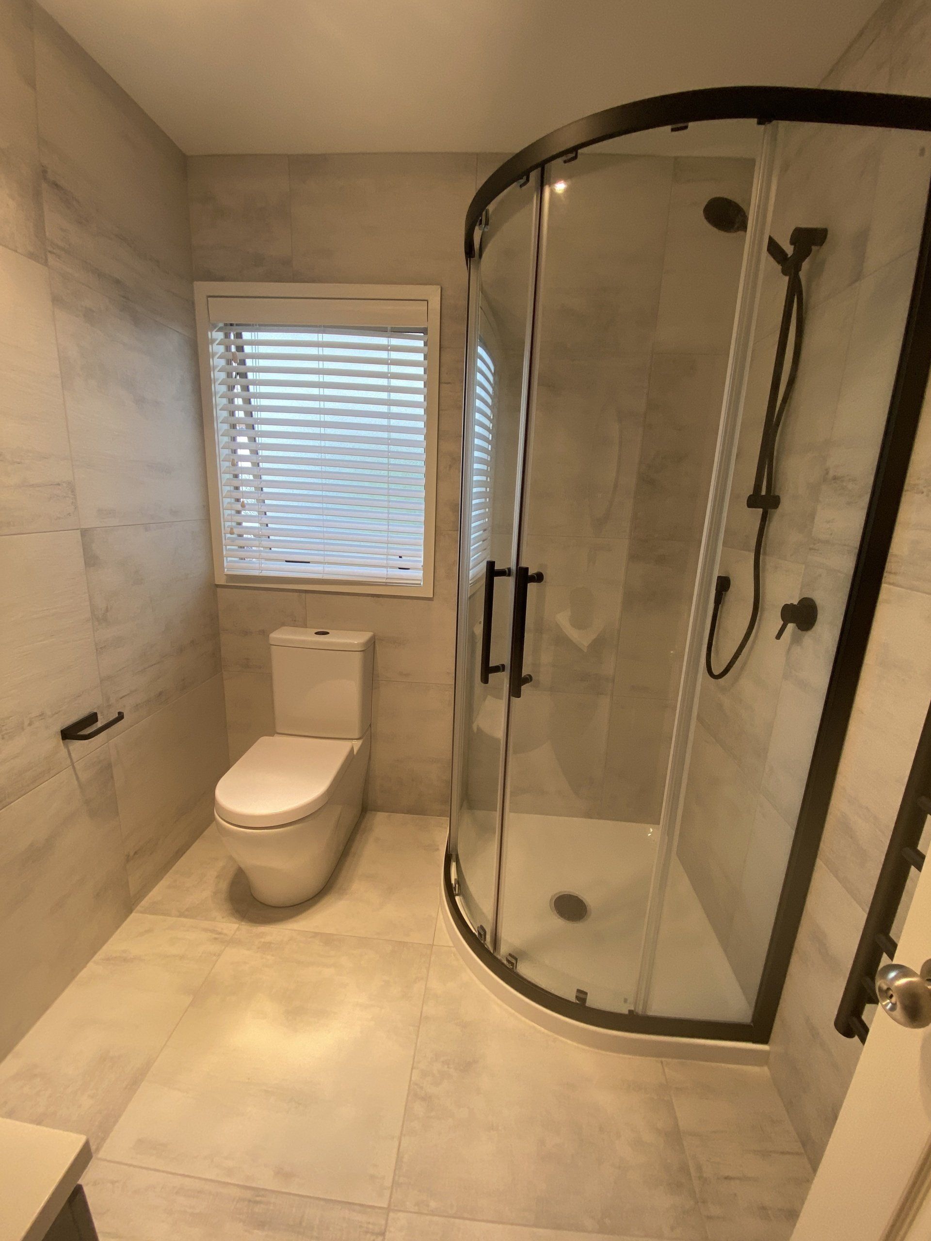 A bathroom with a toilet , shower and window.