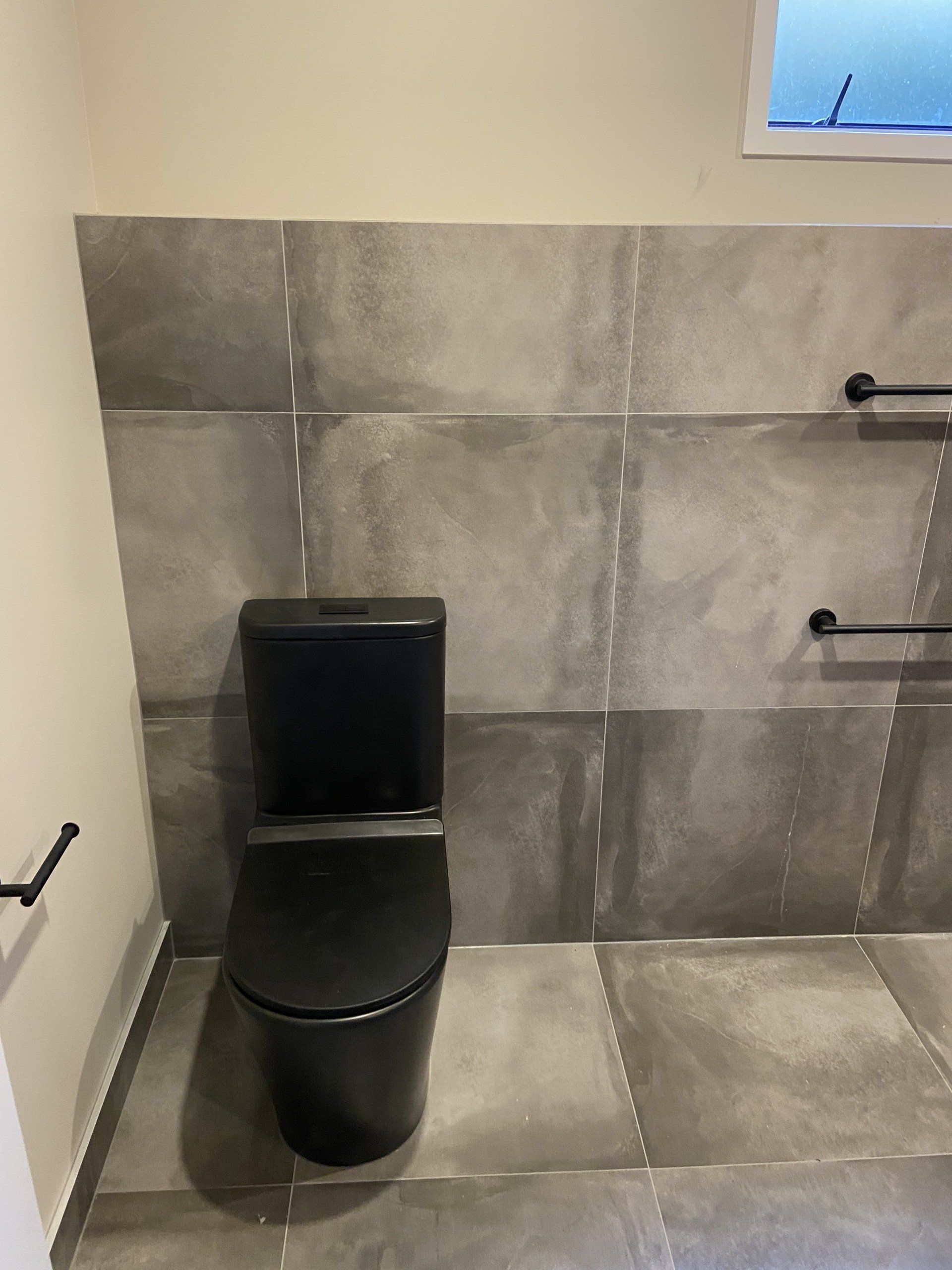 A black toilet is sitting in a bathroom next to a wall.