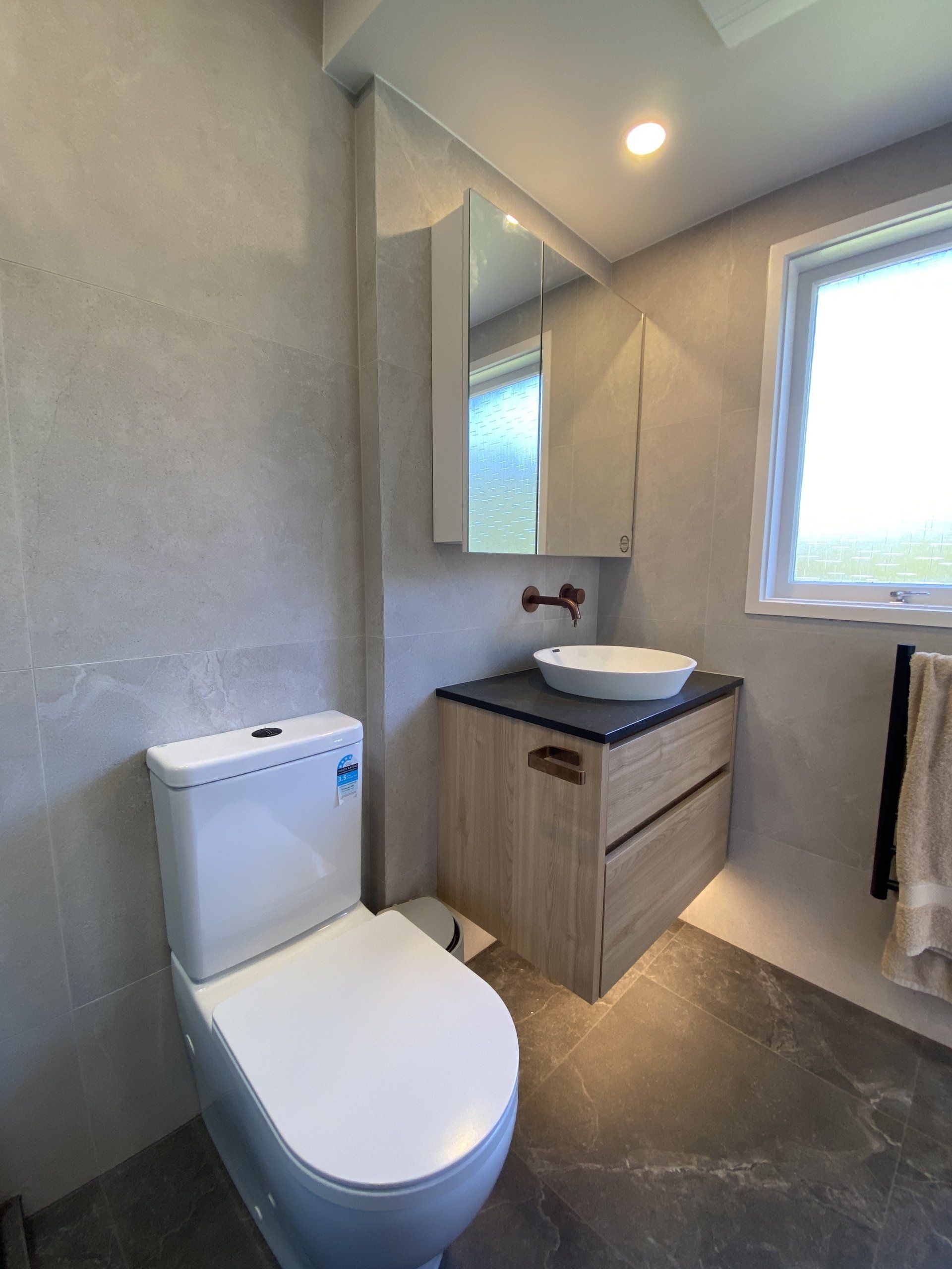 A bathroom with a toilet , sink , mirror and window.