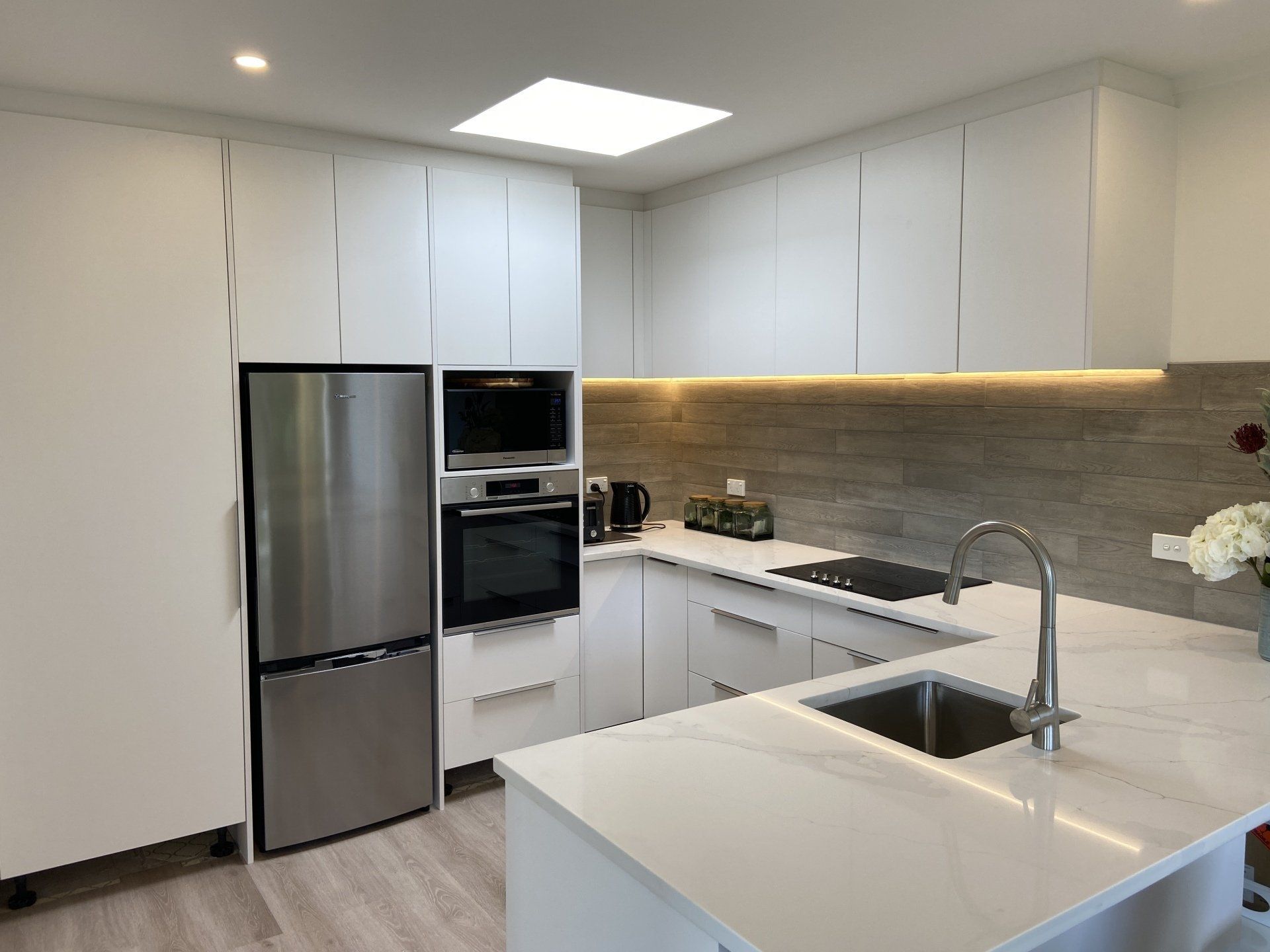 A kitchen with white cabinets , stainless steel appliances , a sink , and a refrigerator.
