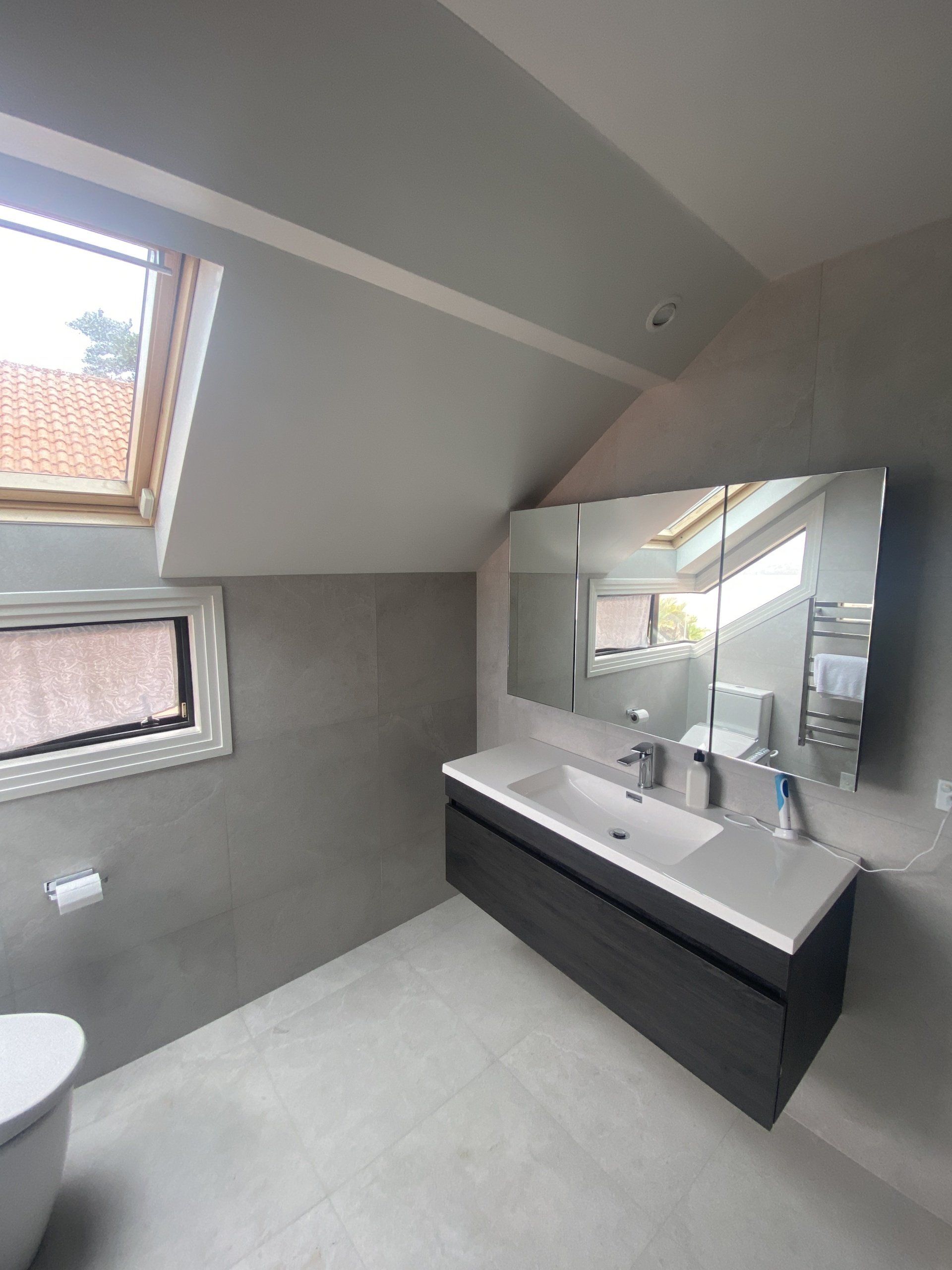 A bathroom with a toilet , sink , mirror and skylight.