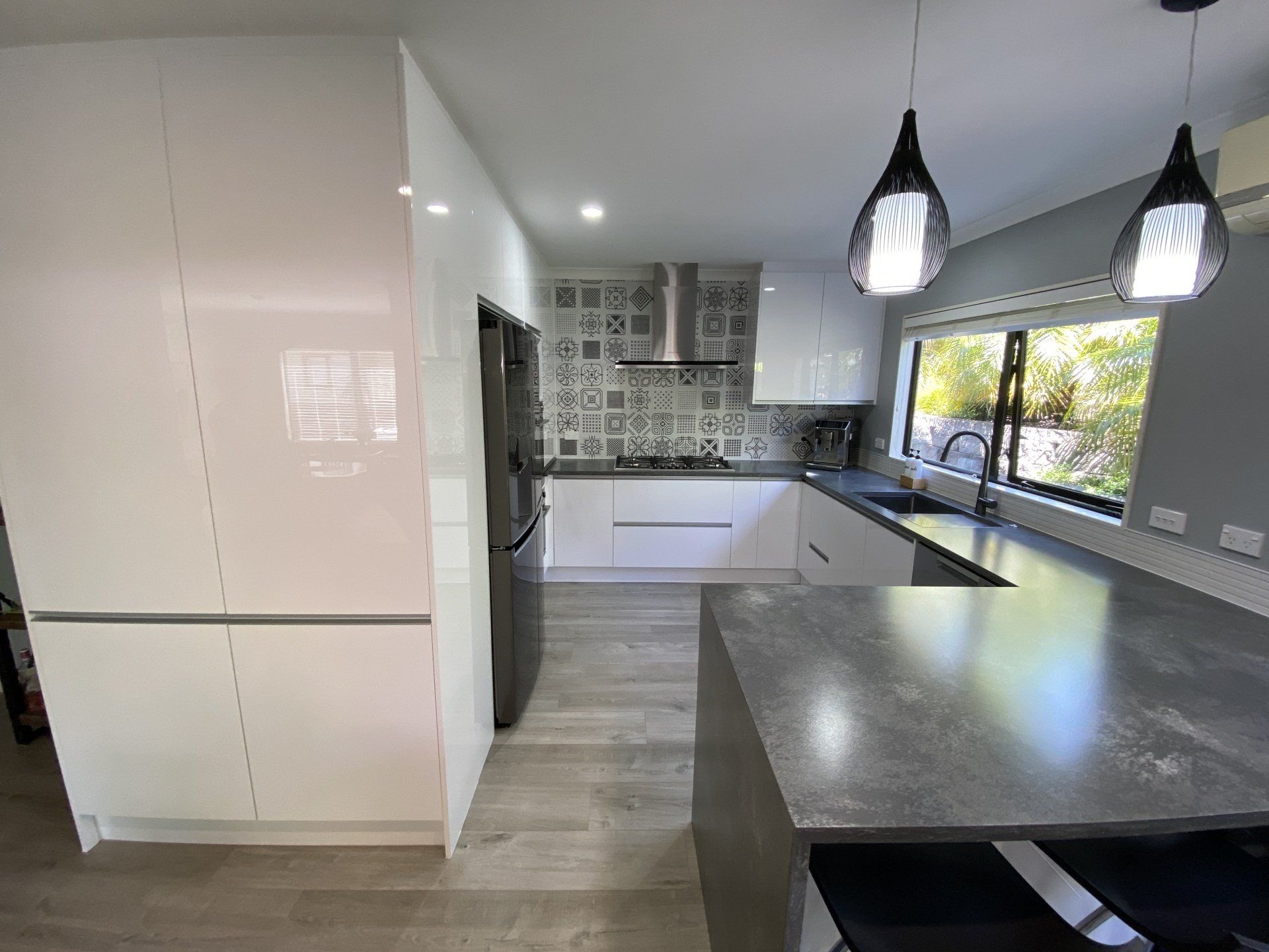 A kitchen with white cabinets , a stainless steel refrigerator , a sink , and a window.