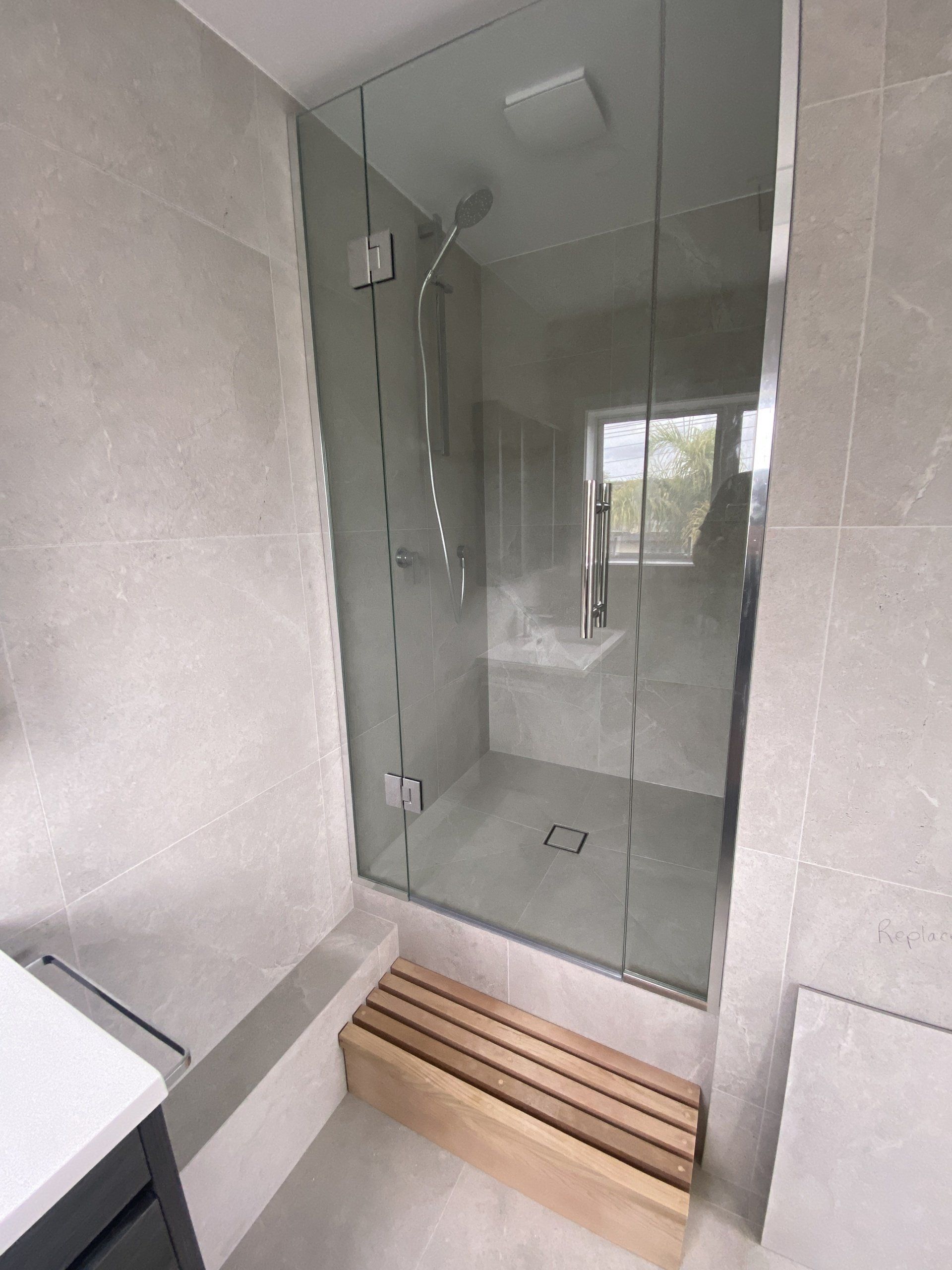 A bathroom with a glass shower door and a wooden bench.