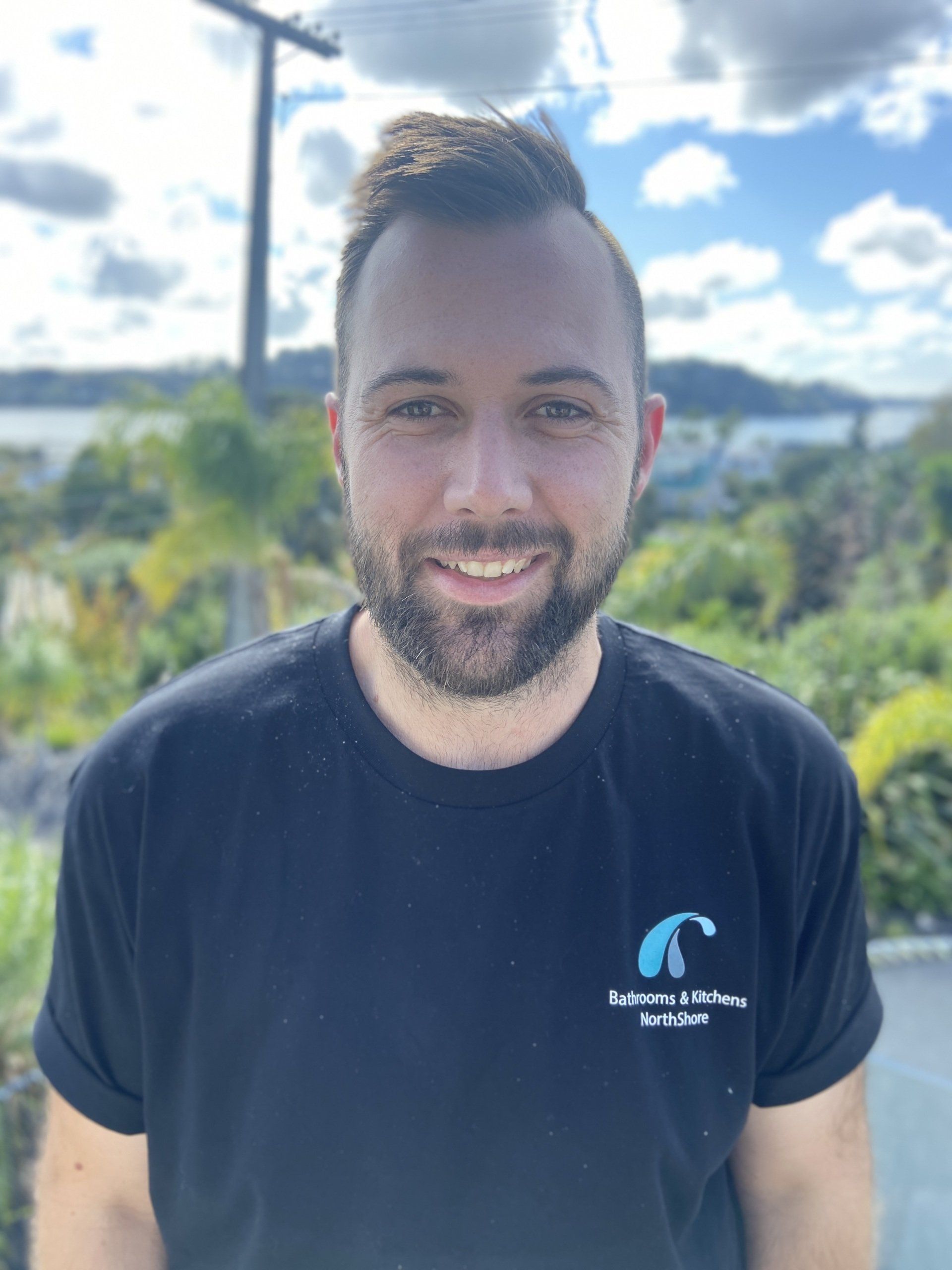 A man with a beard is wearing a black shirt and smiling