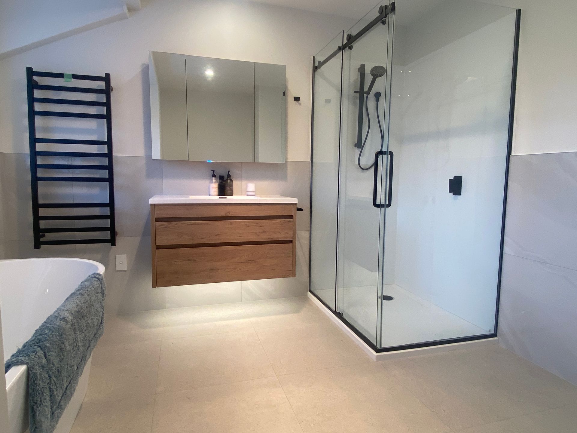 A bathroom with a walk in shower , sink , mirror and towel rack.