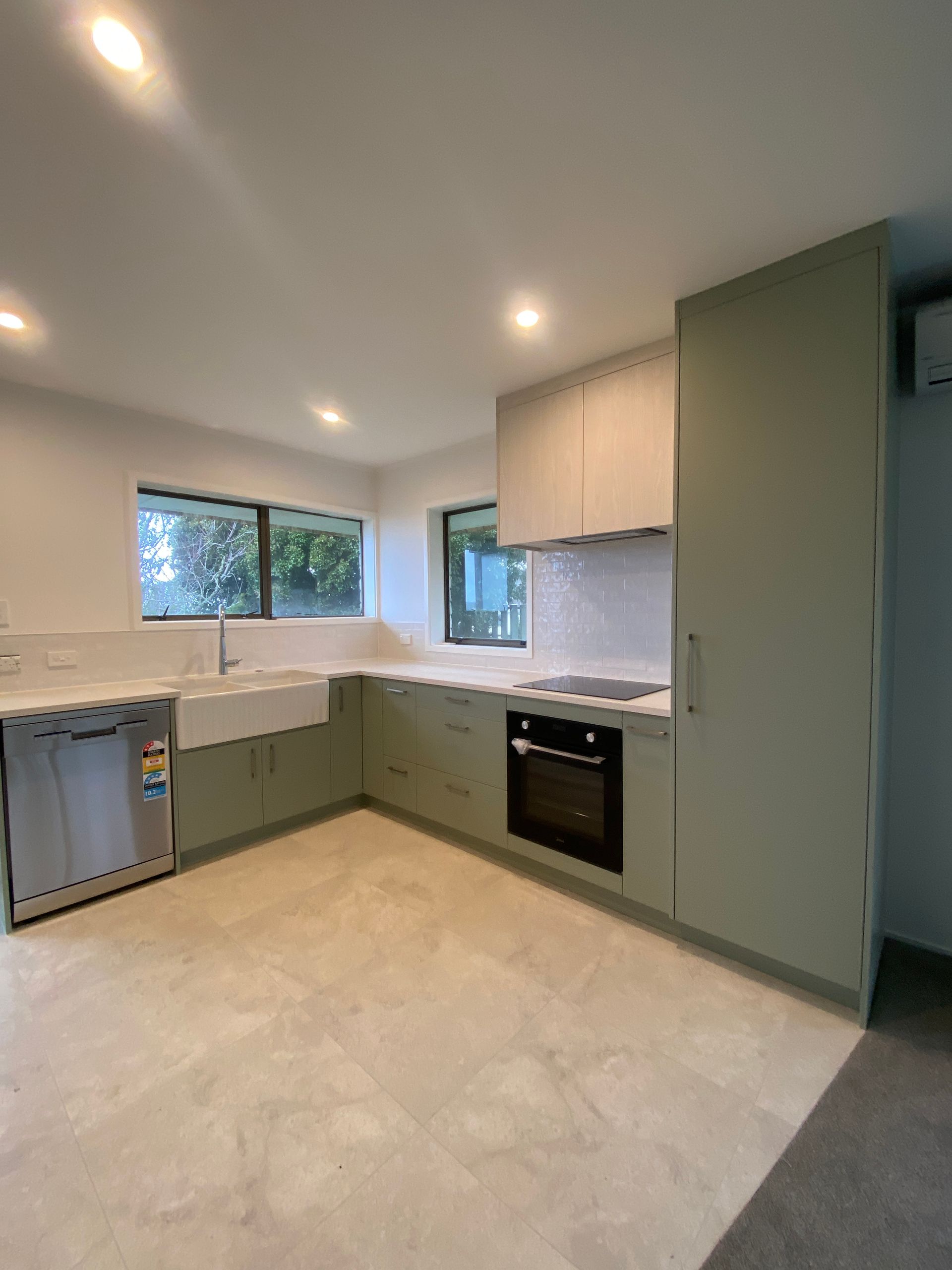 A kitchen with green cabinets , stainless steel appliances , a sink , and a window.