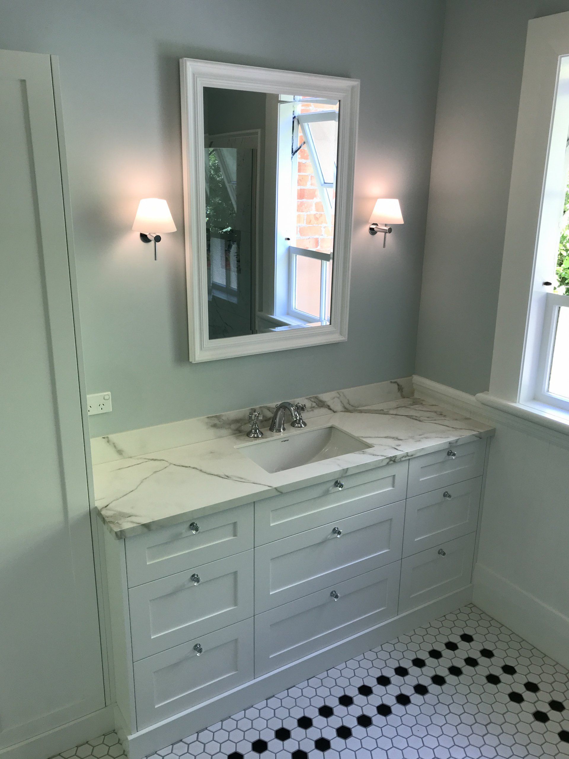 A bathroom with a sink , mirror and window.