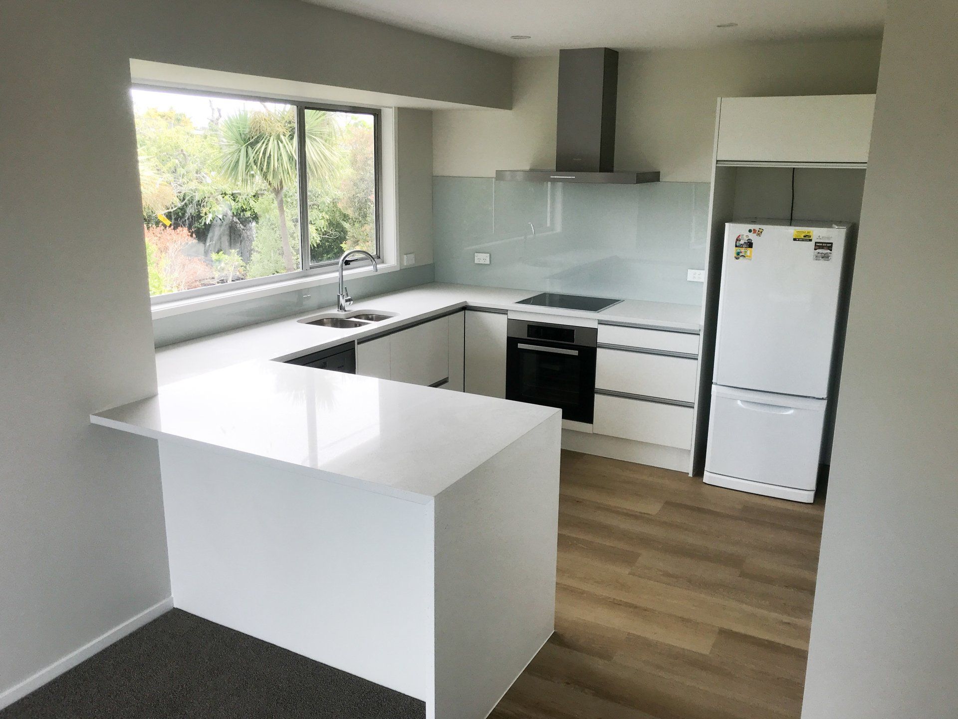 A kitchen with white cabinets , a refrigerator , a sink , and a window.