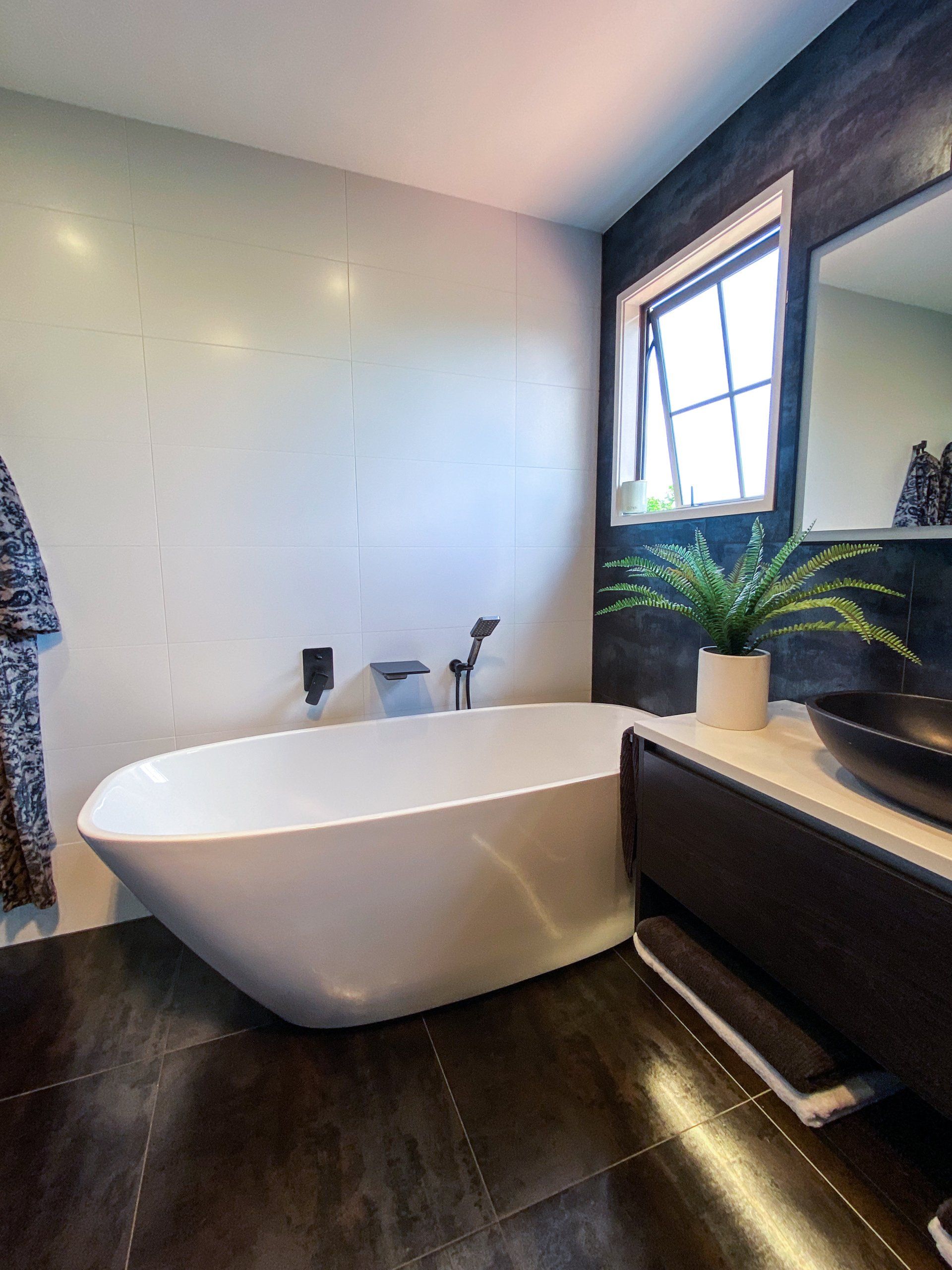 A bathroom with a bathtub , sink , mirror and window.
