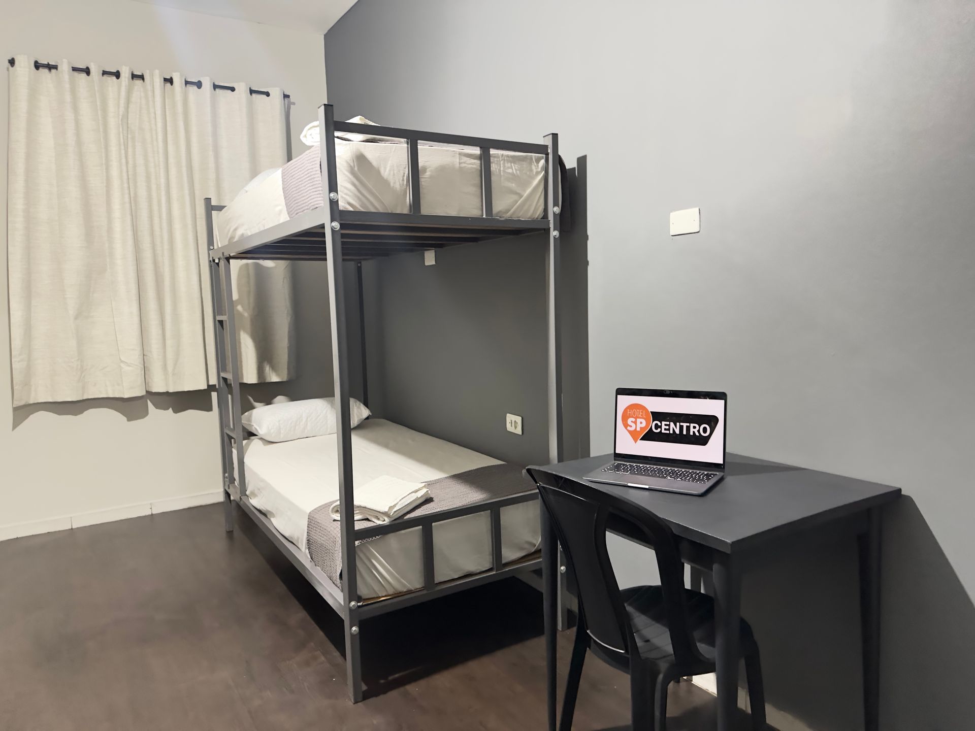 Beliches em um quarto cinza com uma escrivaninha e um laptop.