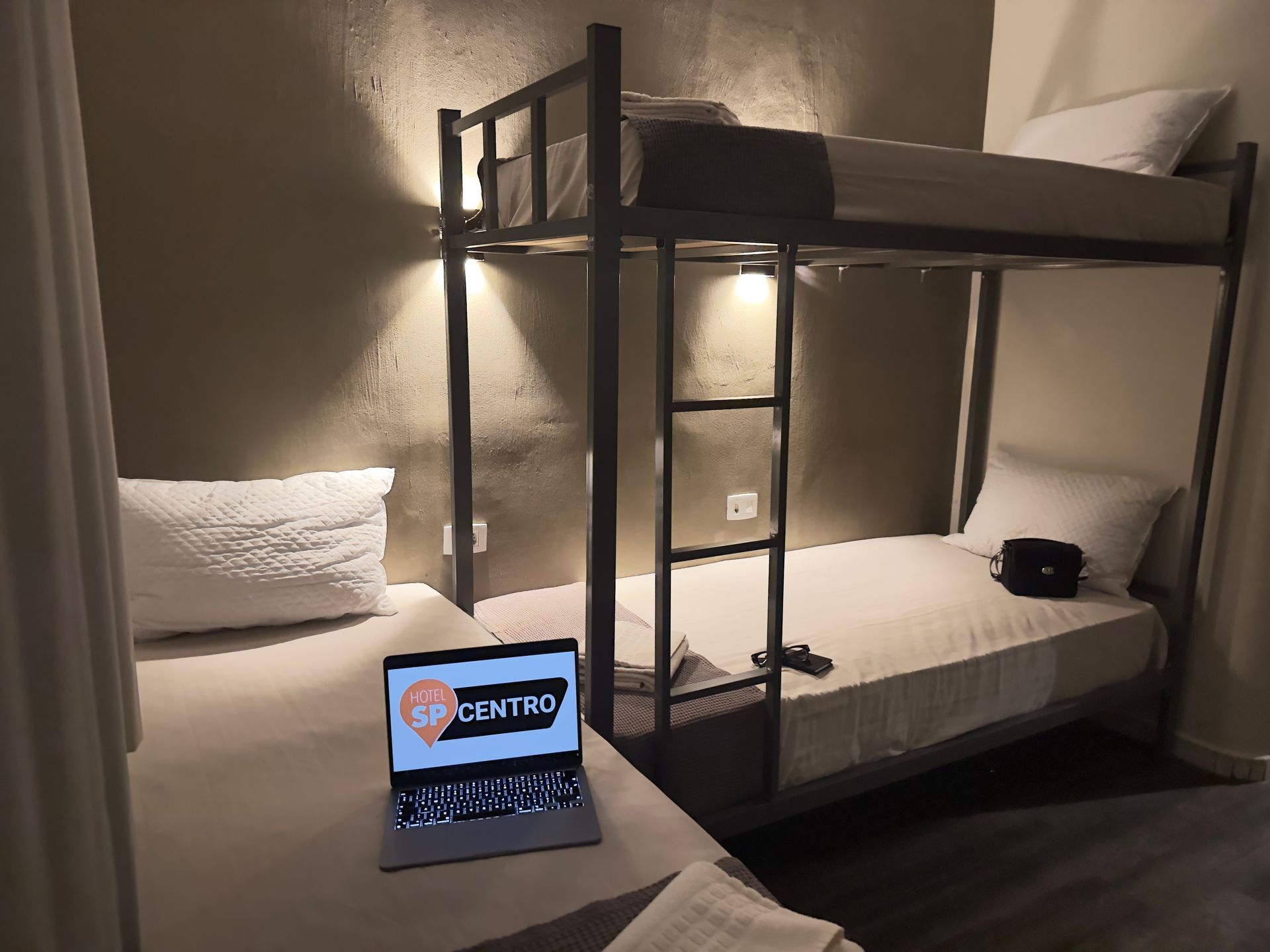 Um quarto com beliches e uma cama com um laptop aberto sobre ela.