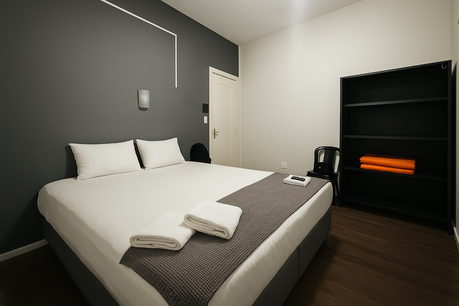 Quarto com parede cinza, cama com roupa de cama branca, toalhas e estante.