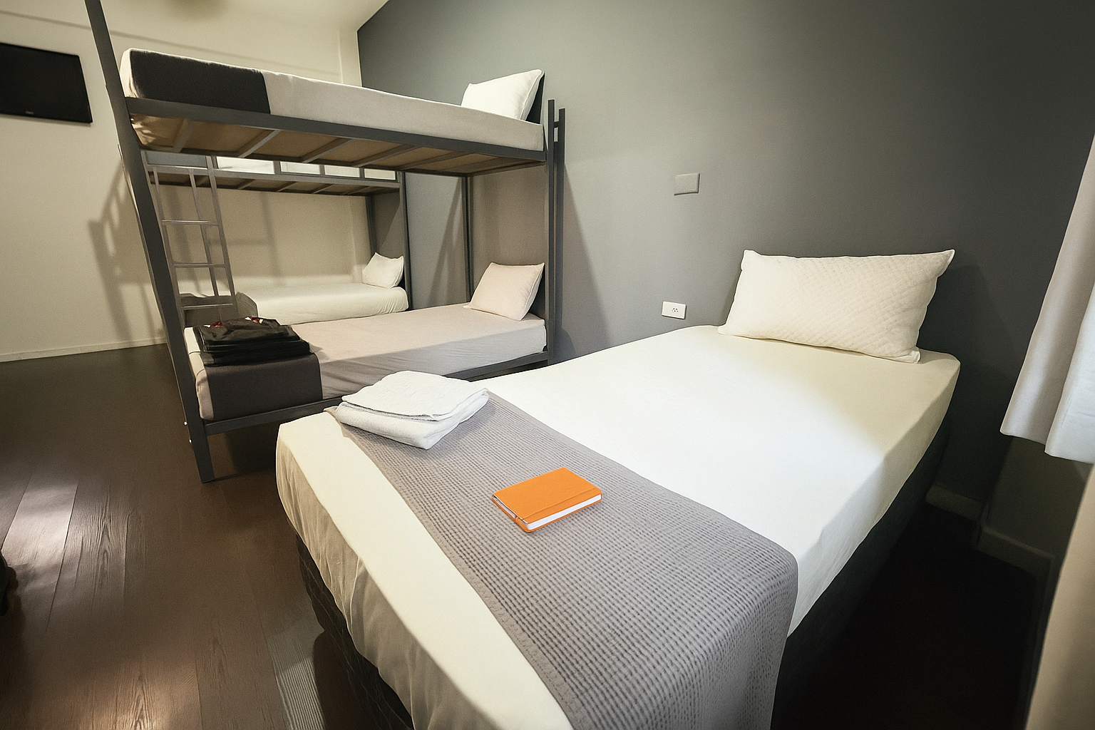 Um quarto de albergue com beliches e uma cama de solteiro, paredes escuras e piso de madeira.