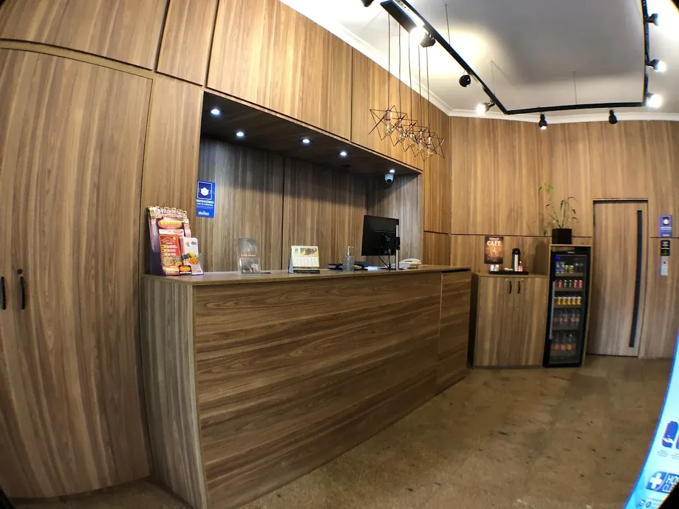 Balcão de recepção em uma sala com revestimento de madeira. Um computador e lanches estão no balcão.