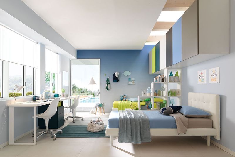 Camera da letto luminosa con letto, scrivania, piante e luce naturale in un appartamento moderno.