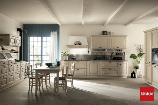 Cucina luminosa color beige con tavolo da pranzo, tende blu e luce del sole che filtra attraverso le porte finestre.
