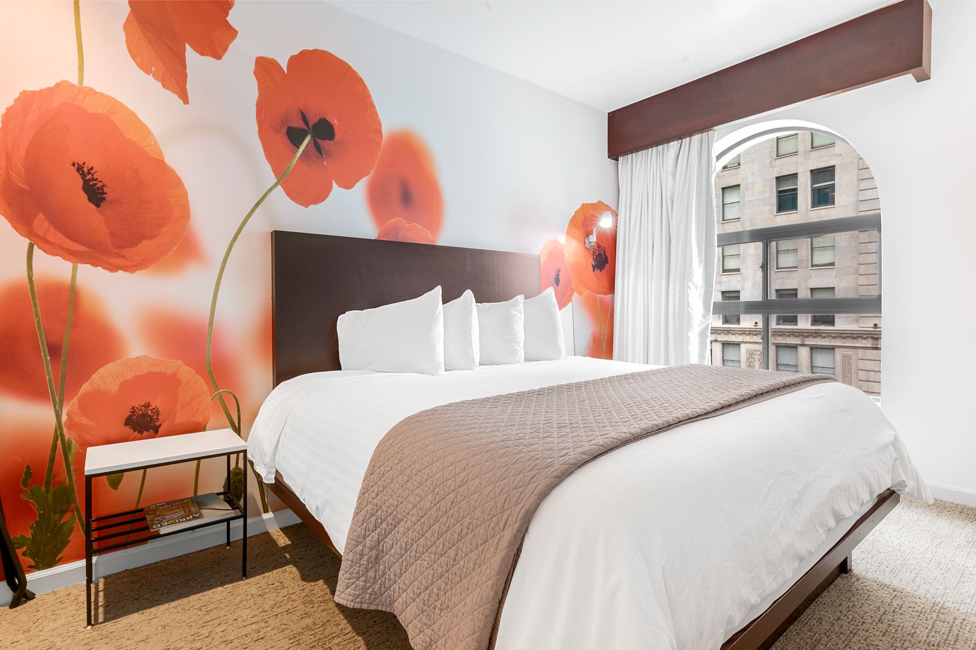 A hotel room with a king size bed and a mural of red flowers on the wall.