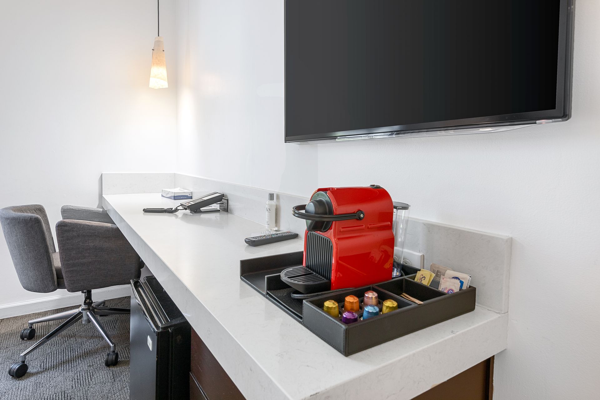 A red coffee maker is sitting on a counter in a hotel room.