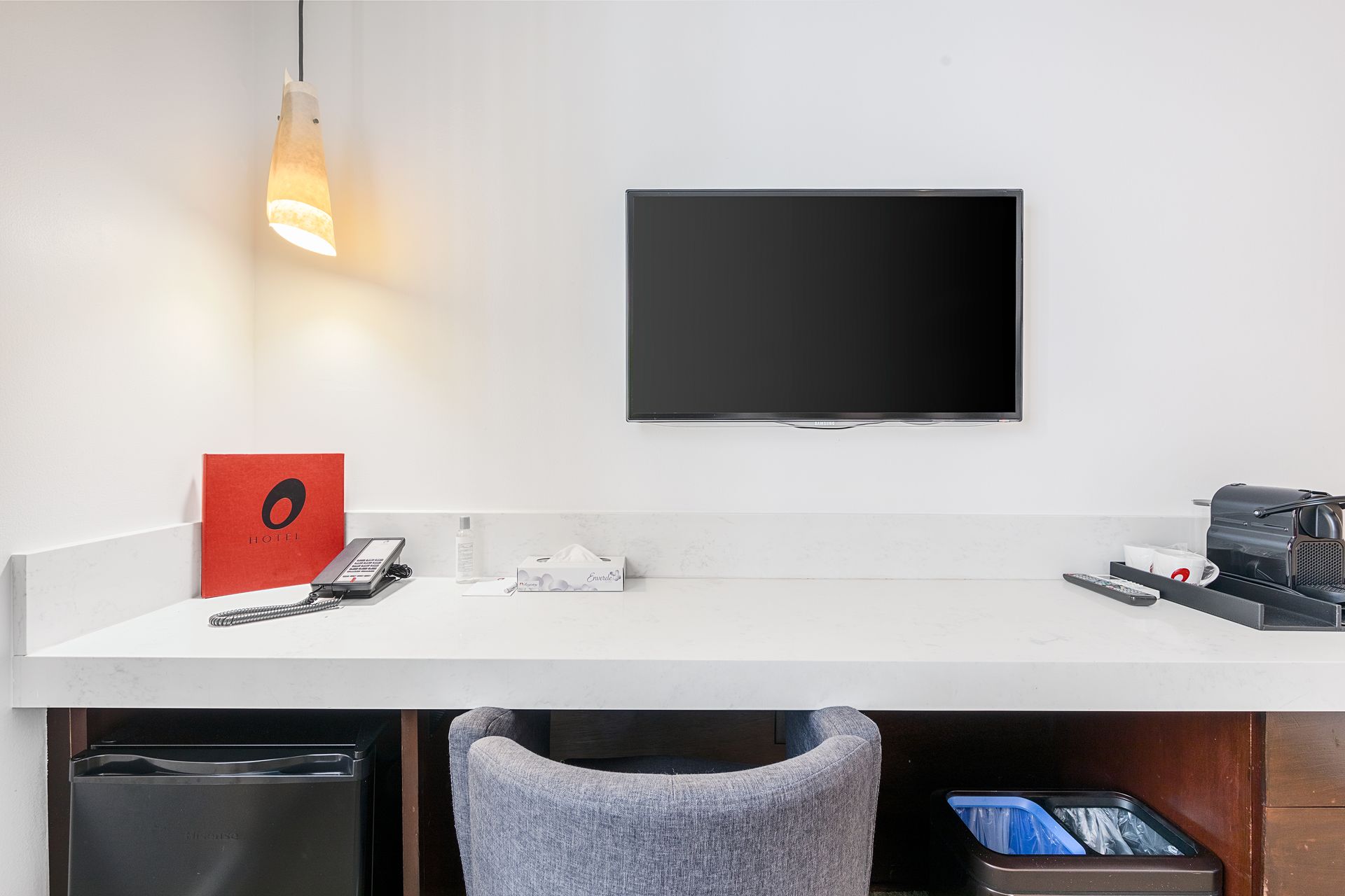 A hotel room with a desk , chair , television and refrigerator.